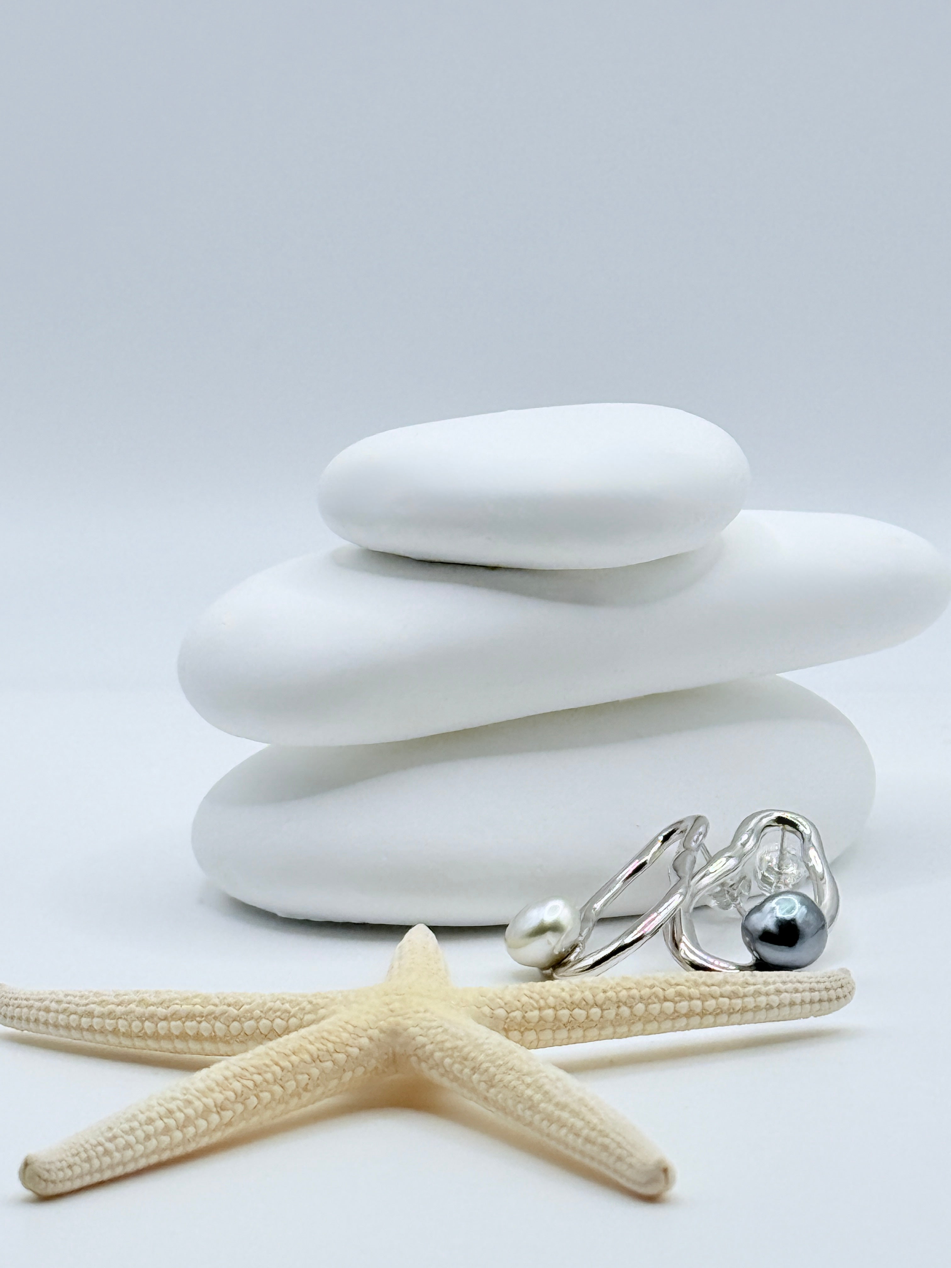 Detailed view of Pebble sterling silver earrings with blue-grey Tahitian and white South Sea keshi pearls on stacked white stones and starfish