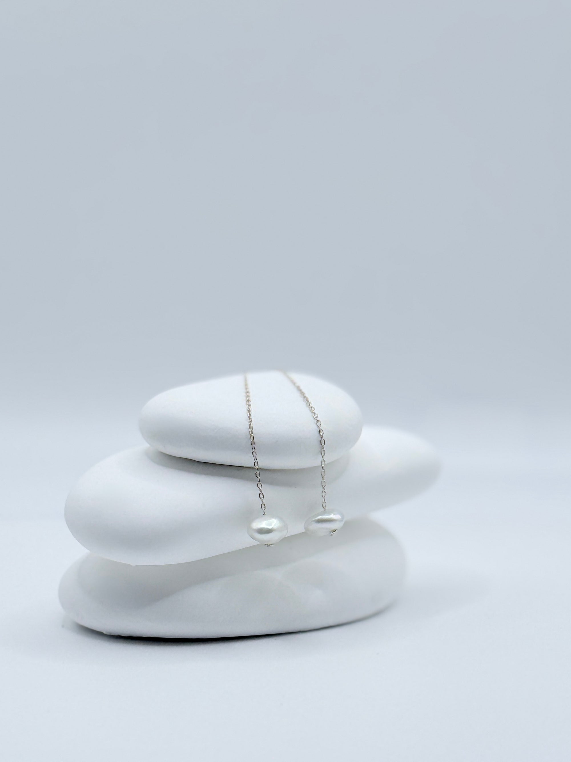 Sterling silver threader earrings with white South Sea keshi pearls displayed on stacked white stones showing delicate chain design