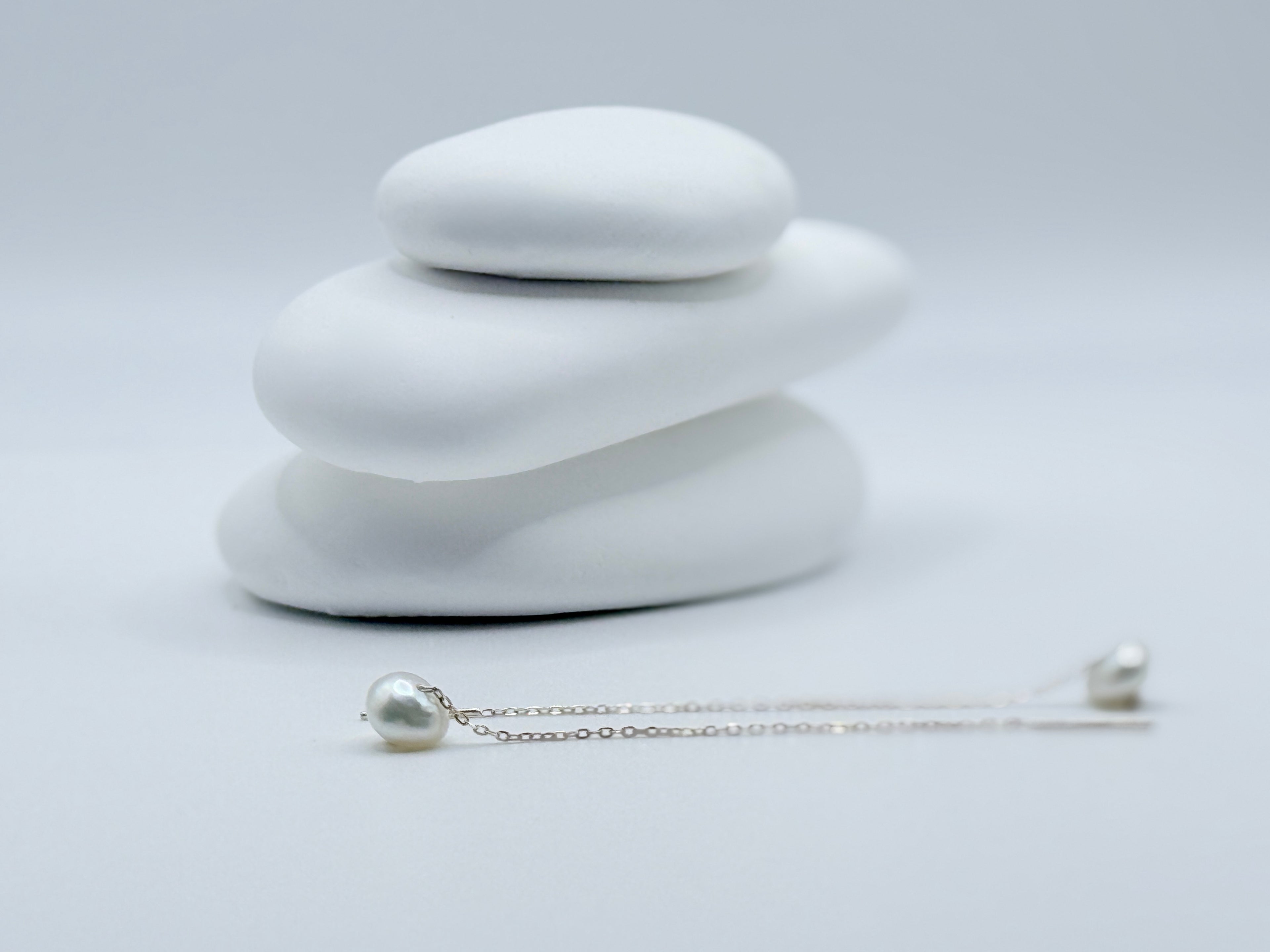 Close-up view of white South Sea keshi pearl threader earrings on white stones highlighting lustrous baroque shapes and sterling silver chains