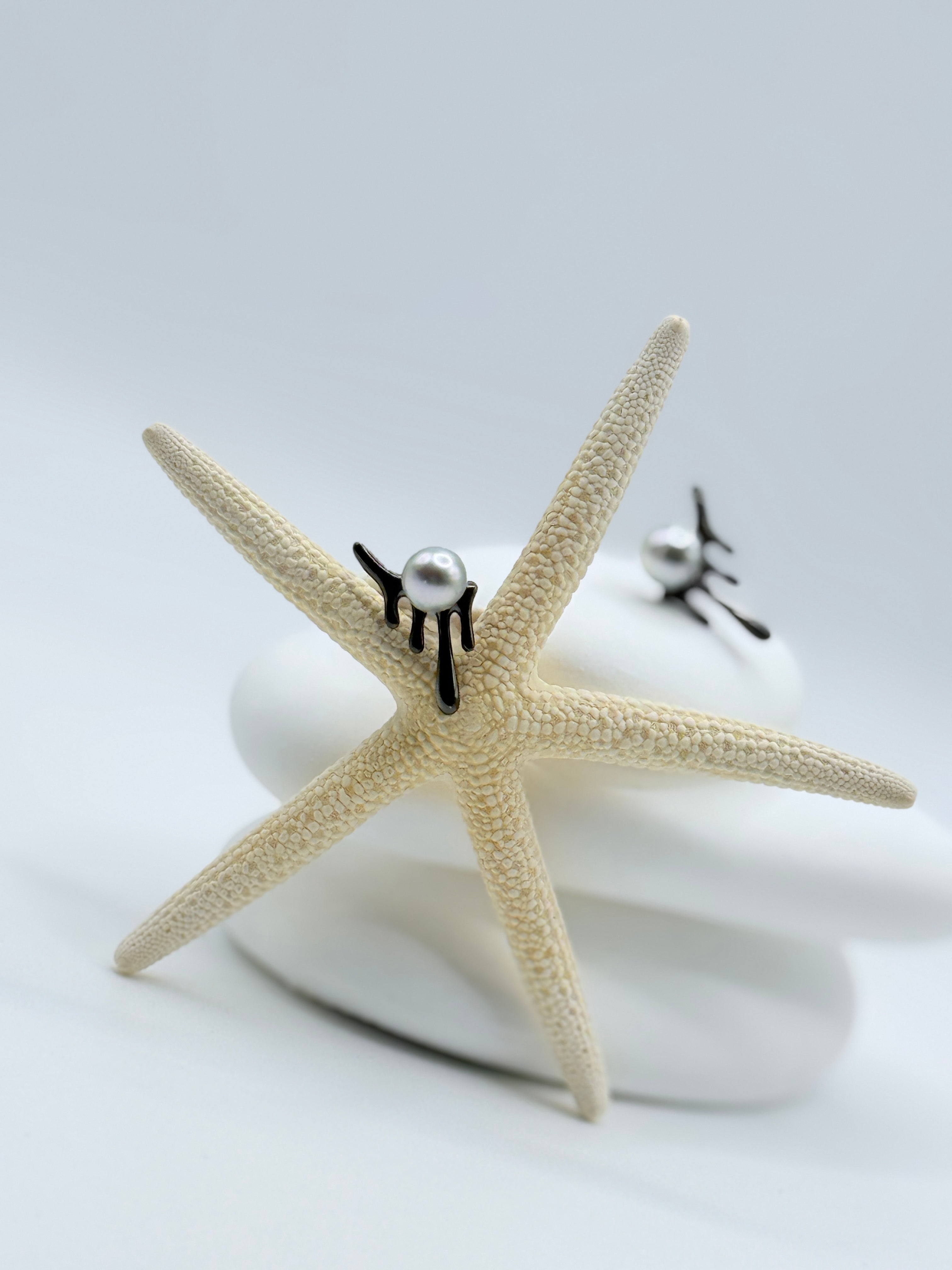 Blackened sterling silver dripping design earrings with light blue Akoya pearls displayed on starfish and white stones showing sculptural form