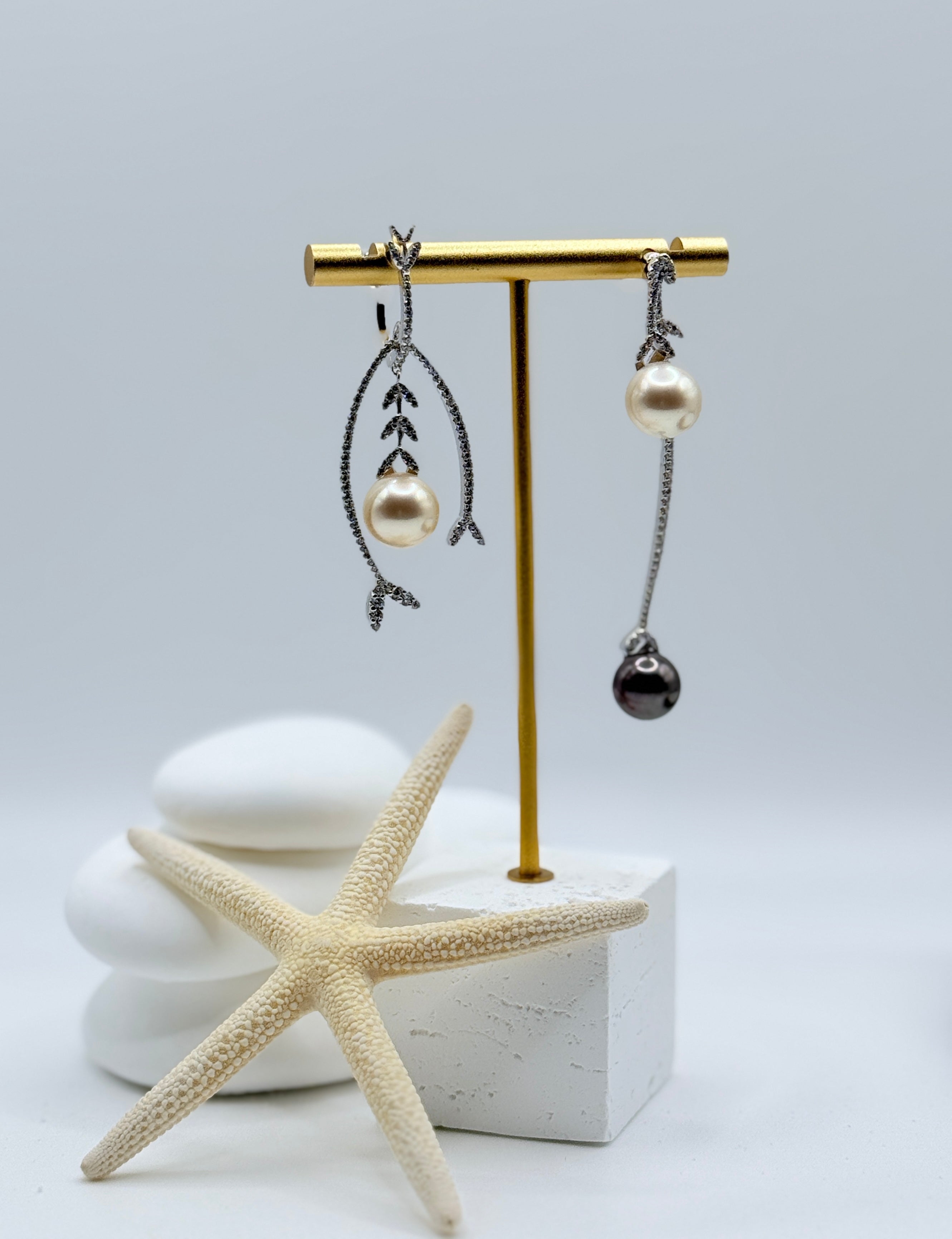 Sterling silver asymmetric earrings with light gold South Sea and black Tahitian pearls displayed on white stones and starfish
