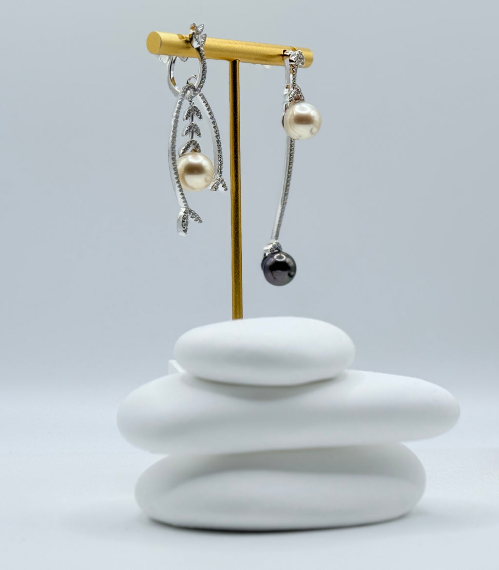 Close-up side view of asymmetric earrings showing intricate leaf design with light gold pearl and sleek black Tahitian pearl on white stones