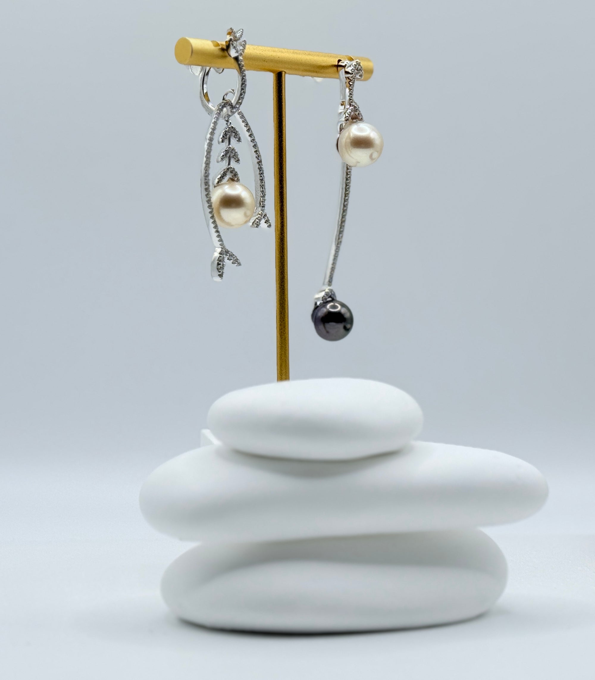 Close-up side view of asymmetric earrings showing intricate leaf design with light gold pearl and sleek black Tahitian pearl on white stones