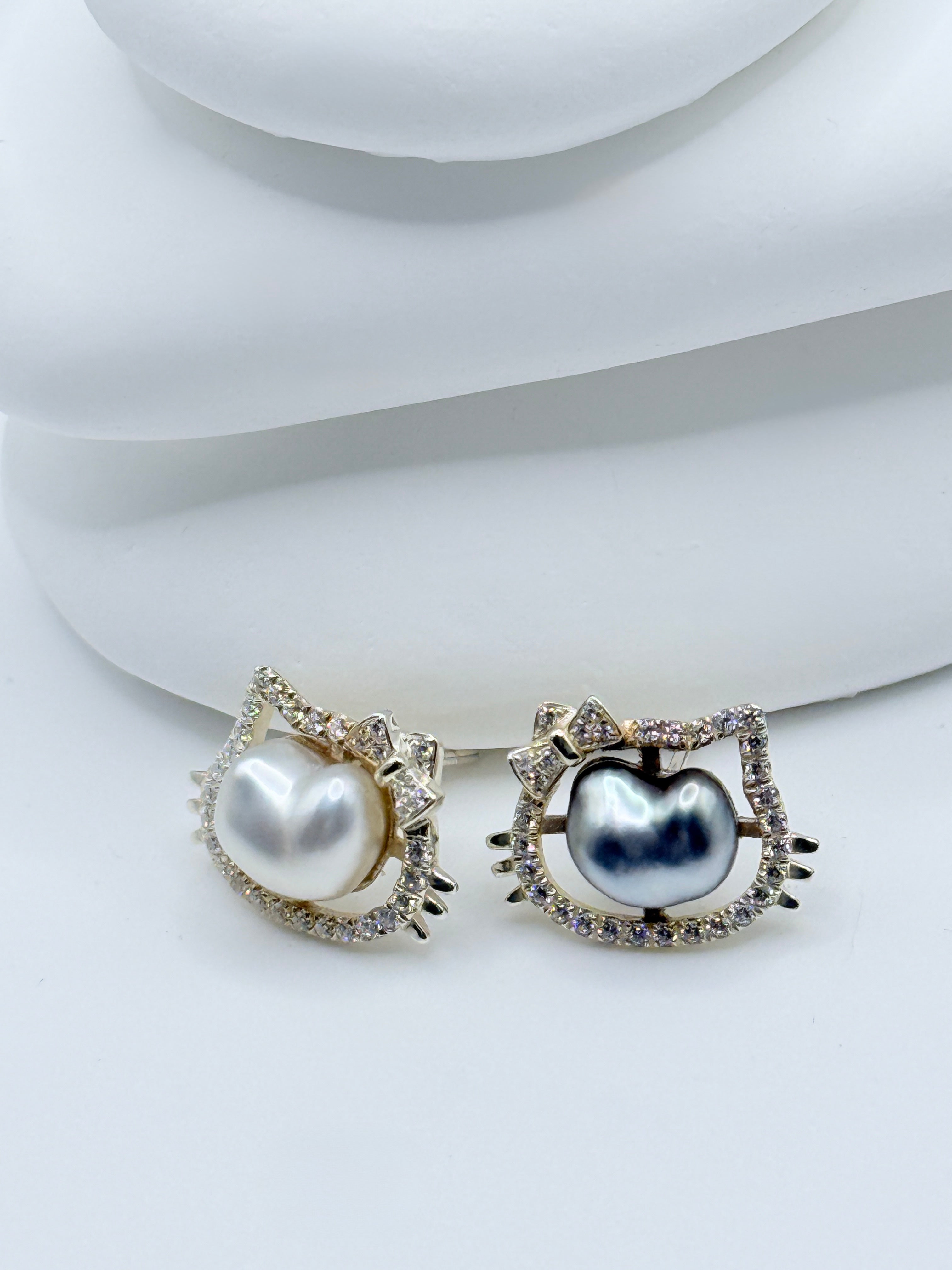 Detailed view of Hello Kitty ear studs showing sterling silver construction with CZ-surrounded keshi pearls on white surface