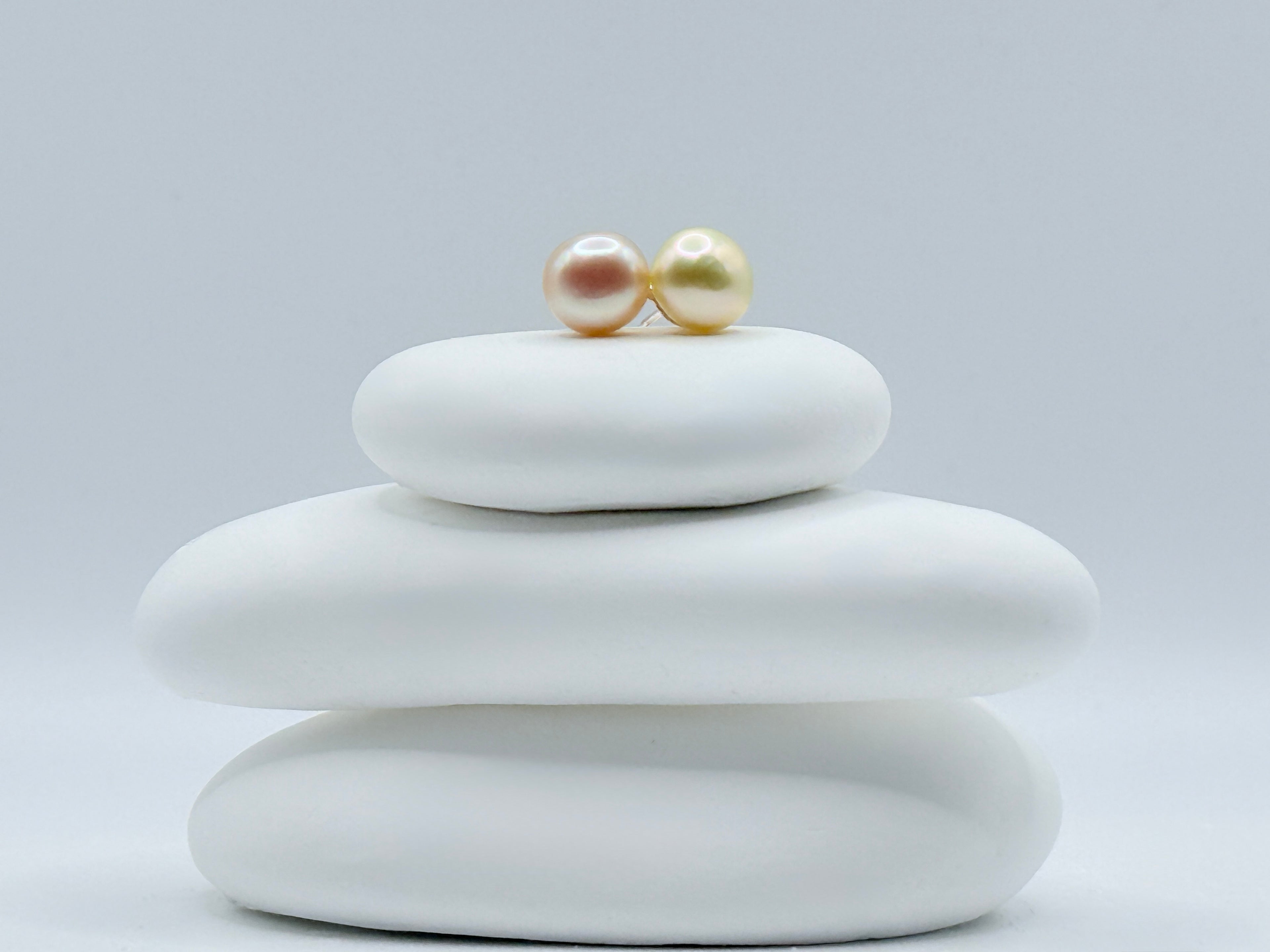 Gold South Sea keshi button pearl ear studs with sterling silver posts and butterfly backs on white stone stack