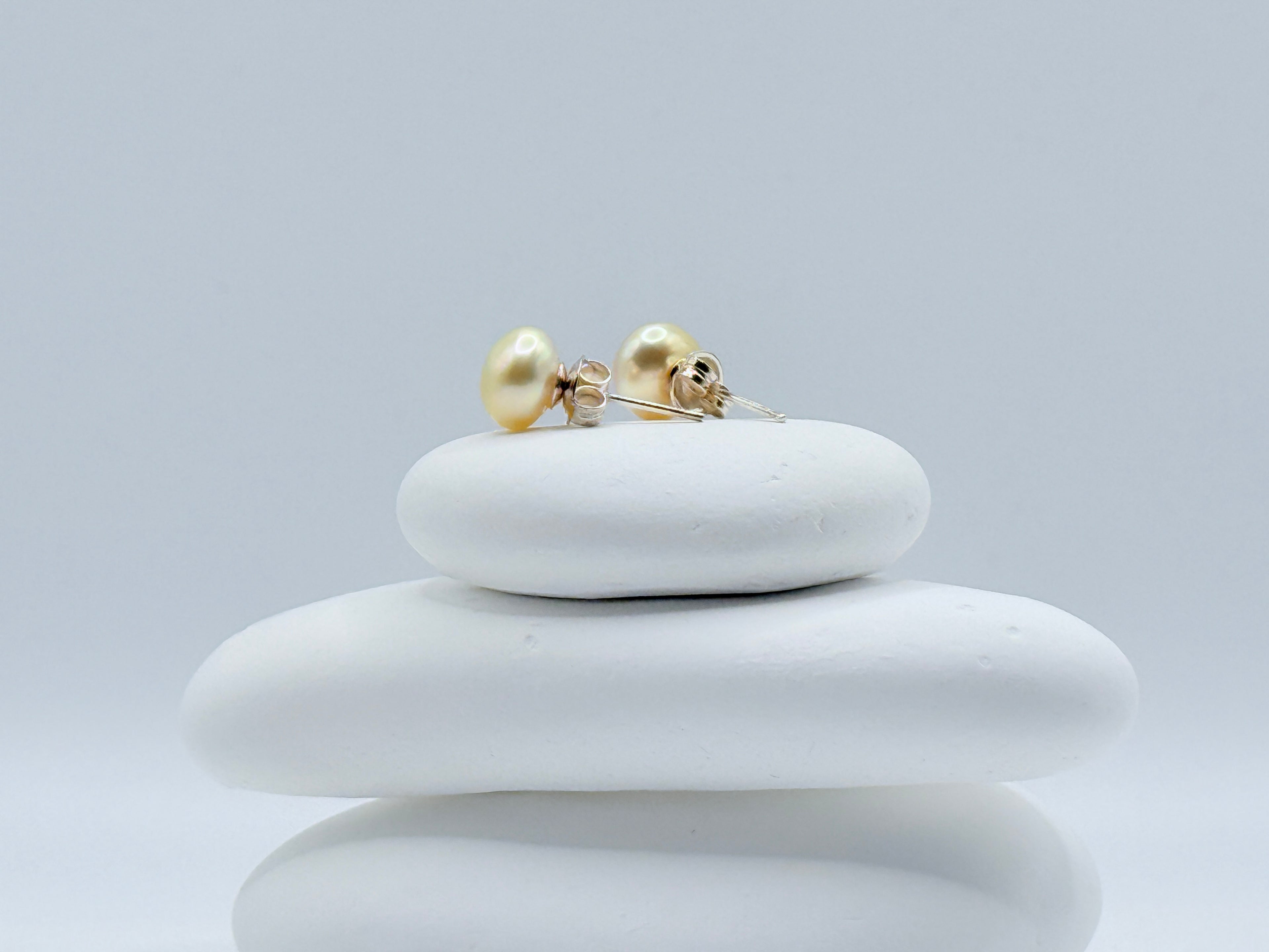 Closure details of sterling silver ear studs with 9mm gold South Sea keshi button pearls displayed on stacked white stones
