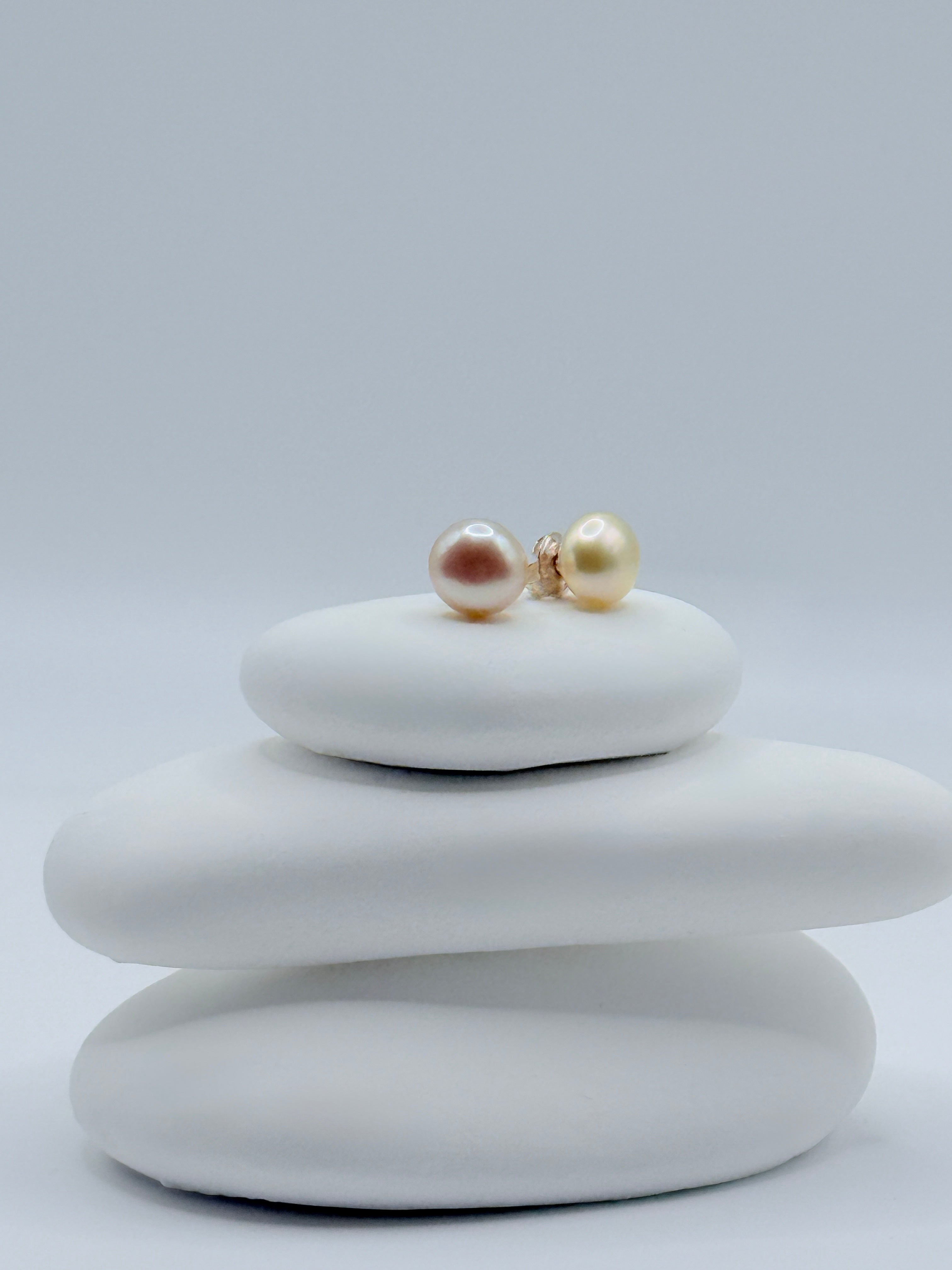 Close-up view of gold South Sea keshi button pearl studs showing warm lustre and sterling silver posts on white stones