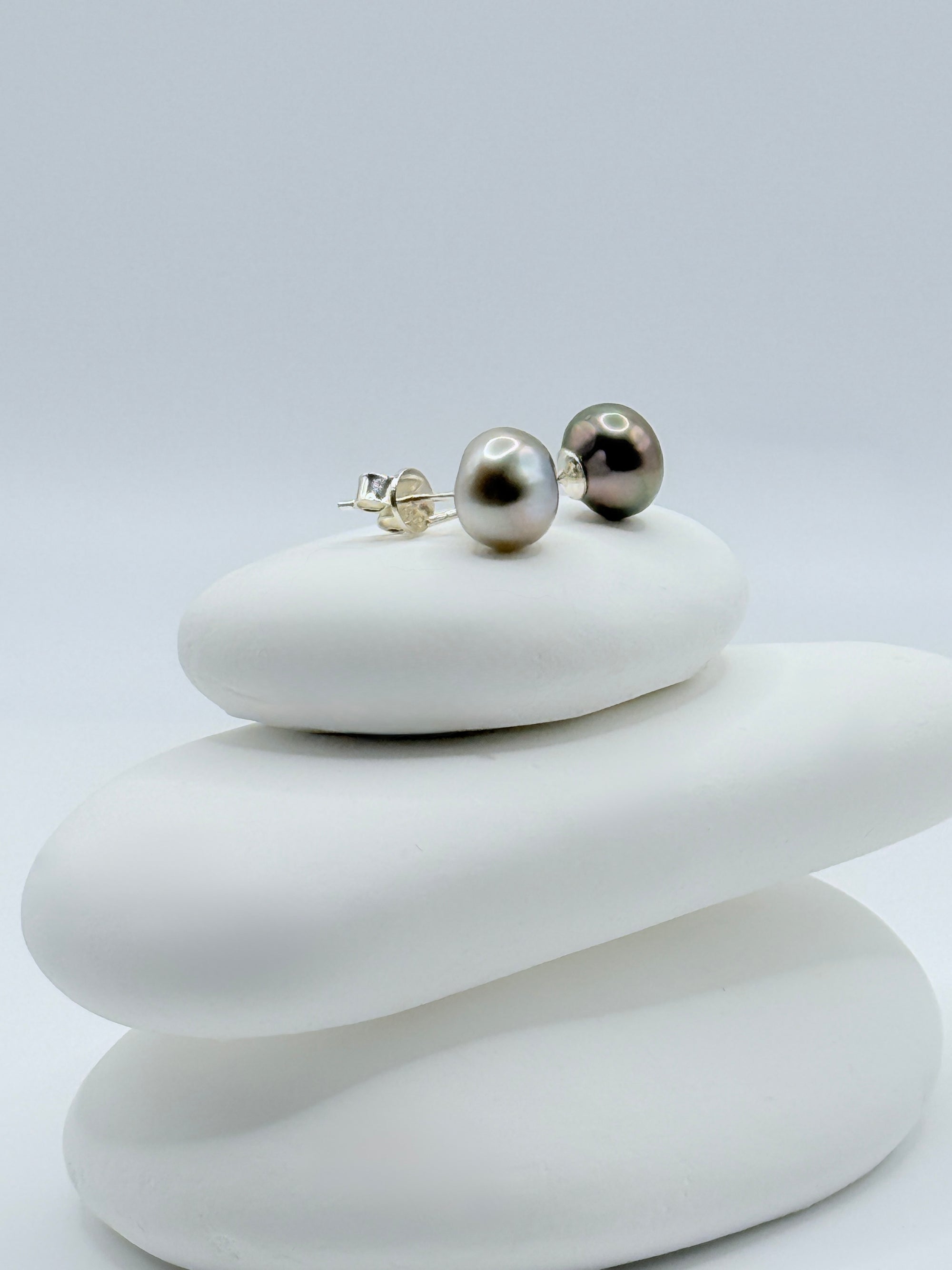 Close-up view of contrasting Tahitian keshi pearl studs showing silver and dark aubergine tones with sterling silver posts on white stones