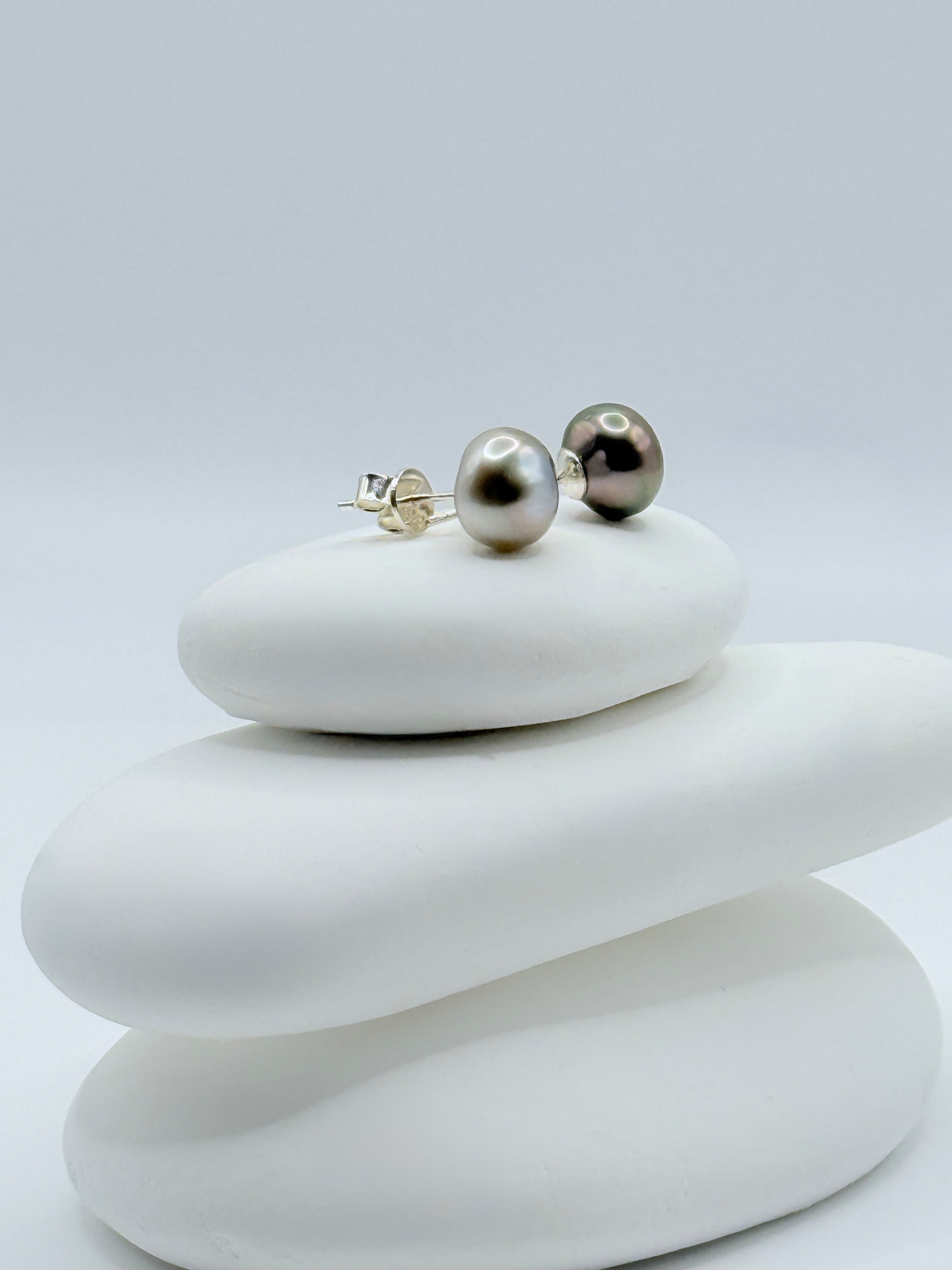 Close-up view of contrasting Tahitian keshi pearl studs showing silver and dark aubergine tones with sterling silver posts on white stones