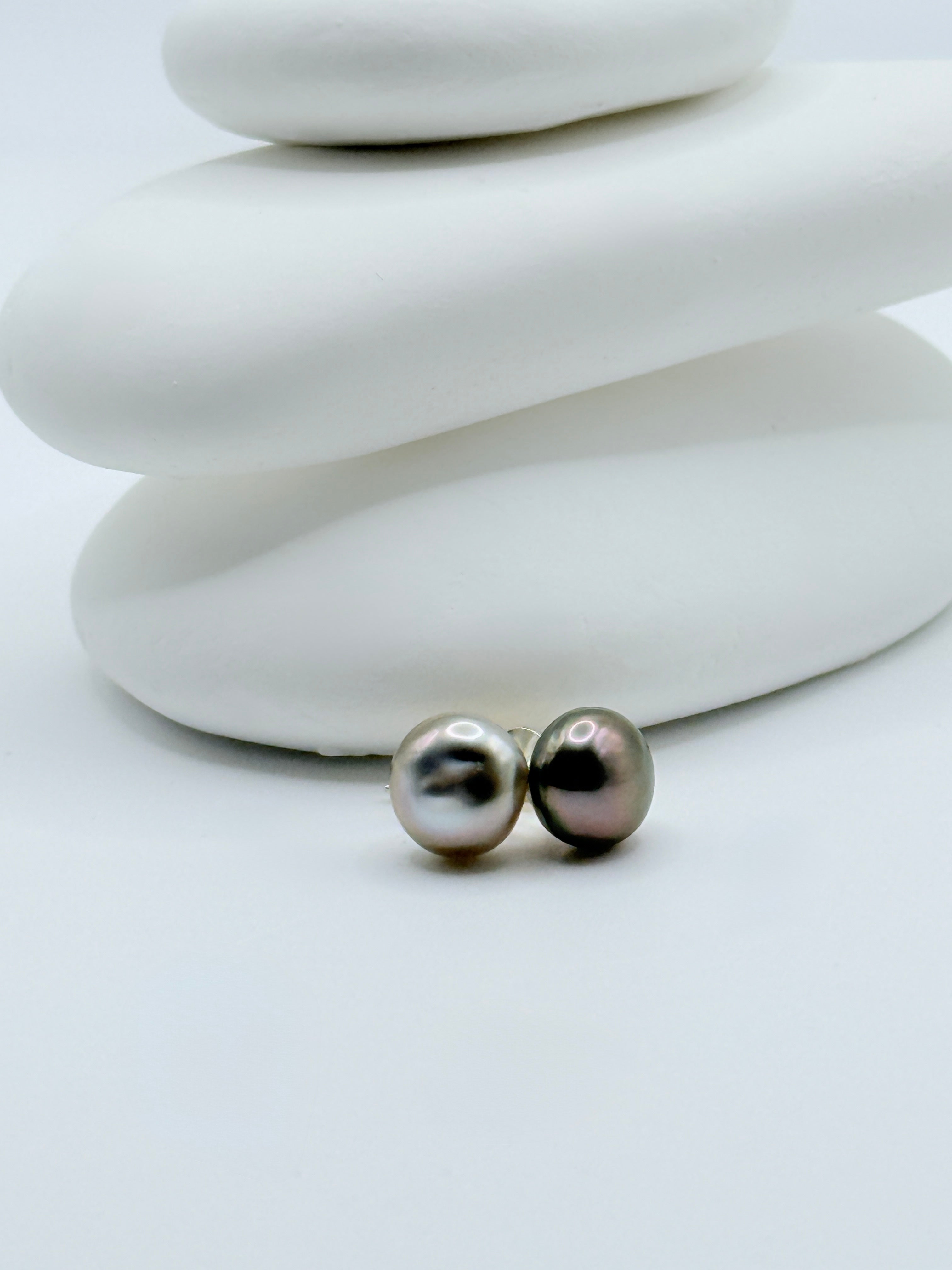 Gambier Island Tahitian keshi pearl ear studs with contrasting silver and aubergine colours displayed on white stone stack