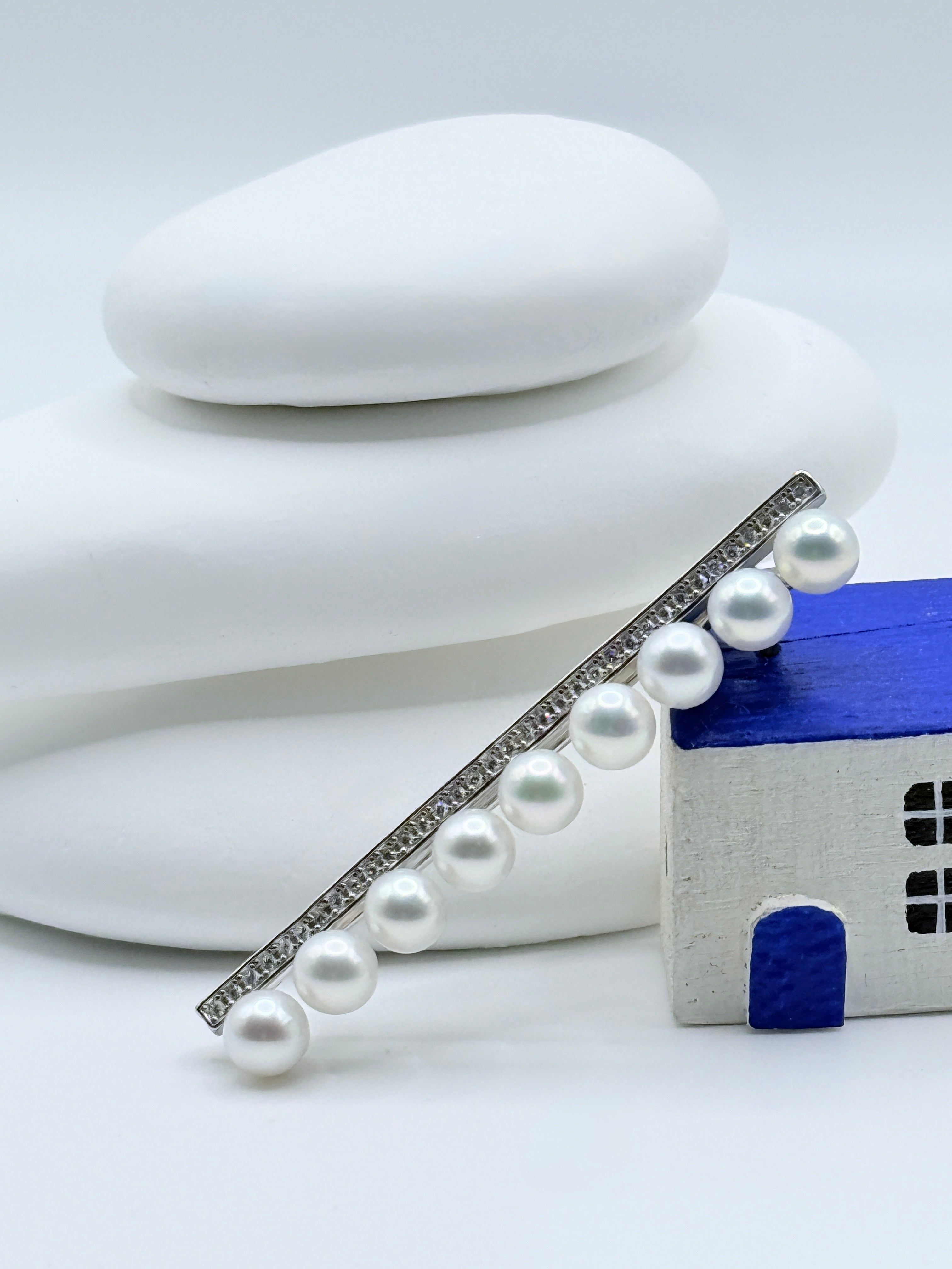 Sterling silver bar pin brooch with 9 white freshwater pearls and trombone clasp mechanism displayed with blue house decoration