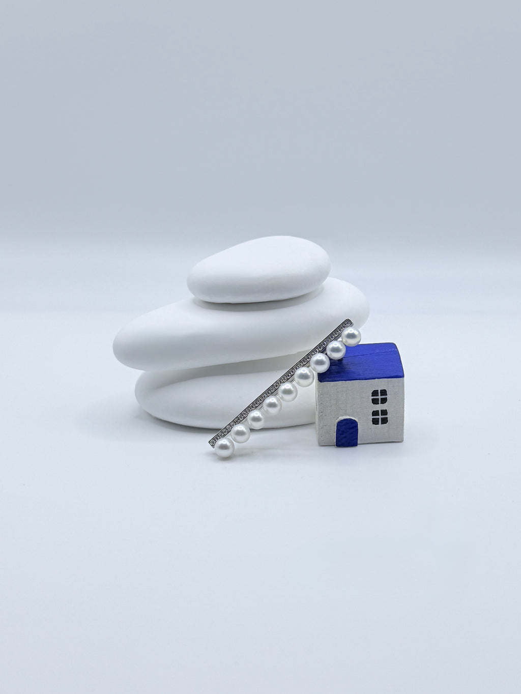 Sterling silver bar pin brooch with 9 white freshwater pearls and pavé CZ details displayed with decorative house on white stones