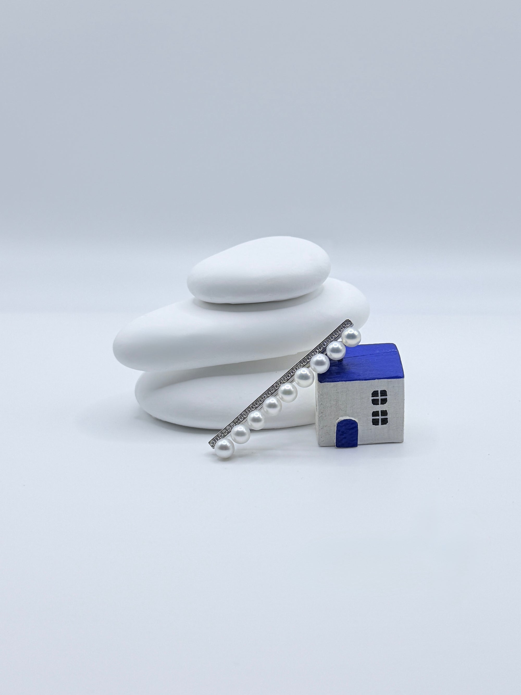 Sterling silver bar pin brooch with 9 white freshwater pearls and pavé CZ details displayed with decorative house on white stones
