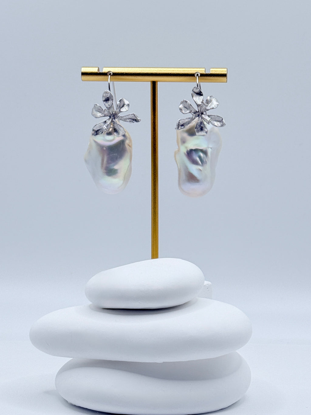 Sterling silver 2-way convertible dangle earrings with large baroque freshwater pearls and floral details displayed on gold earring stand