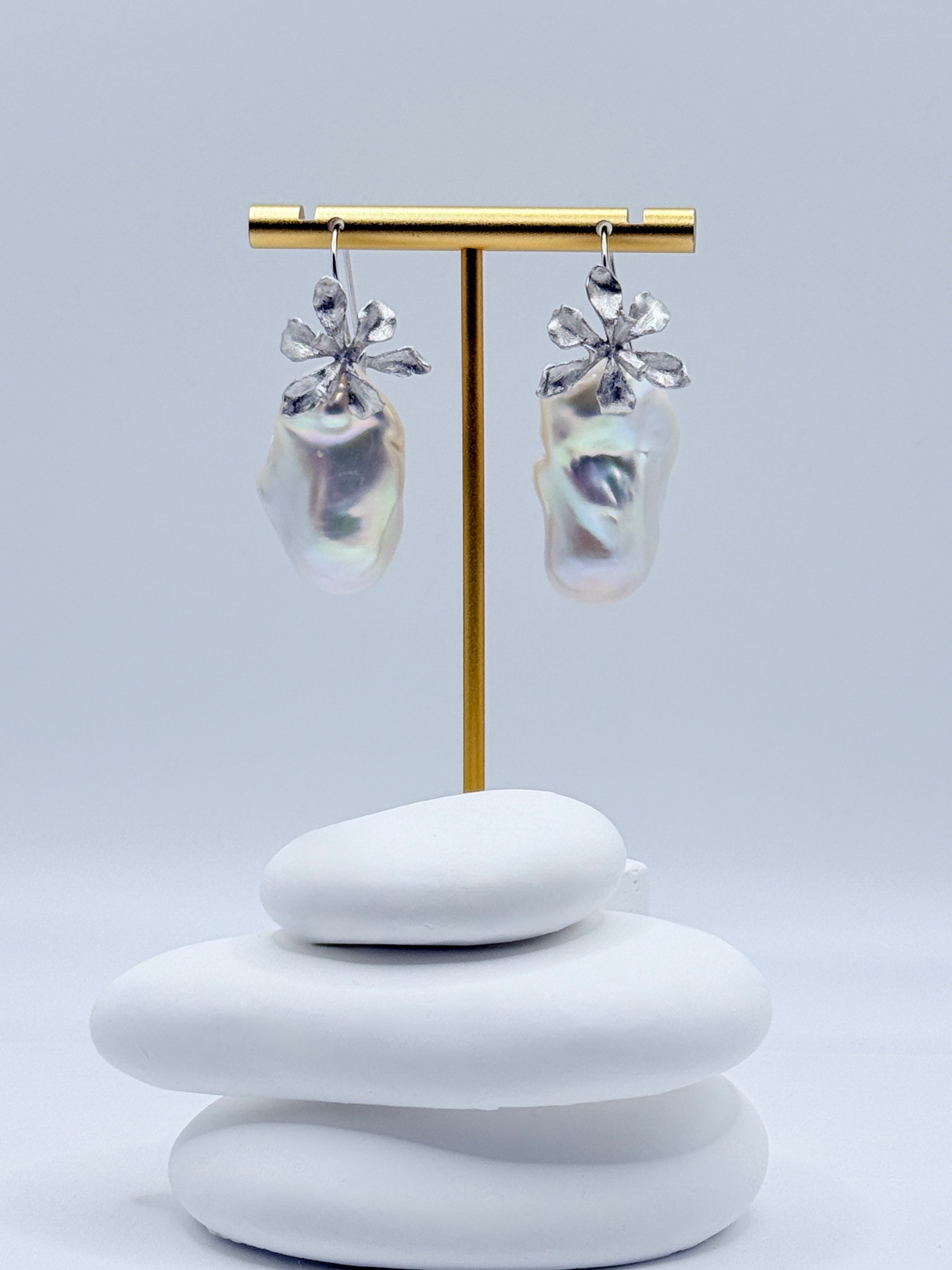 Sterling silver 2-way convertible dangle earrings with large baroque freshwater pearls and floral details displayed on gold earring stand