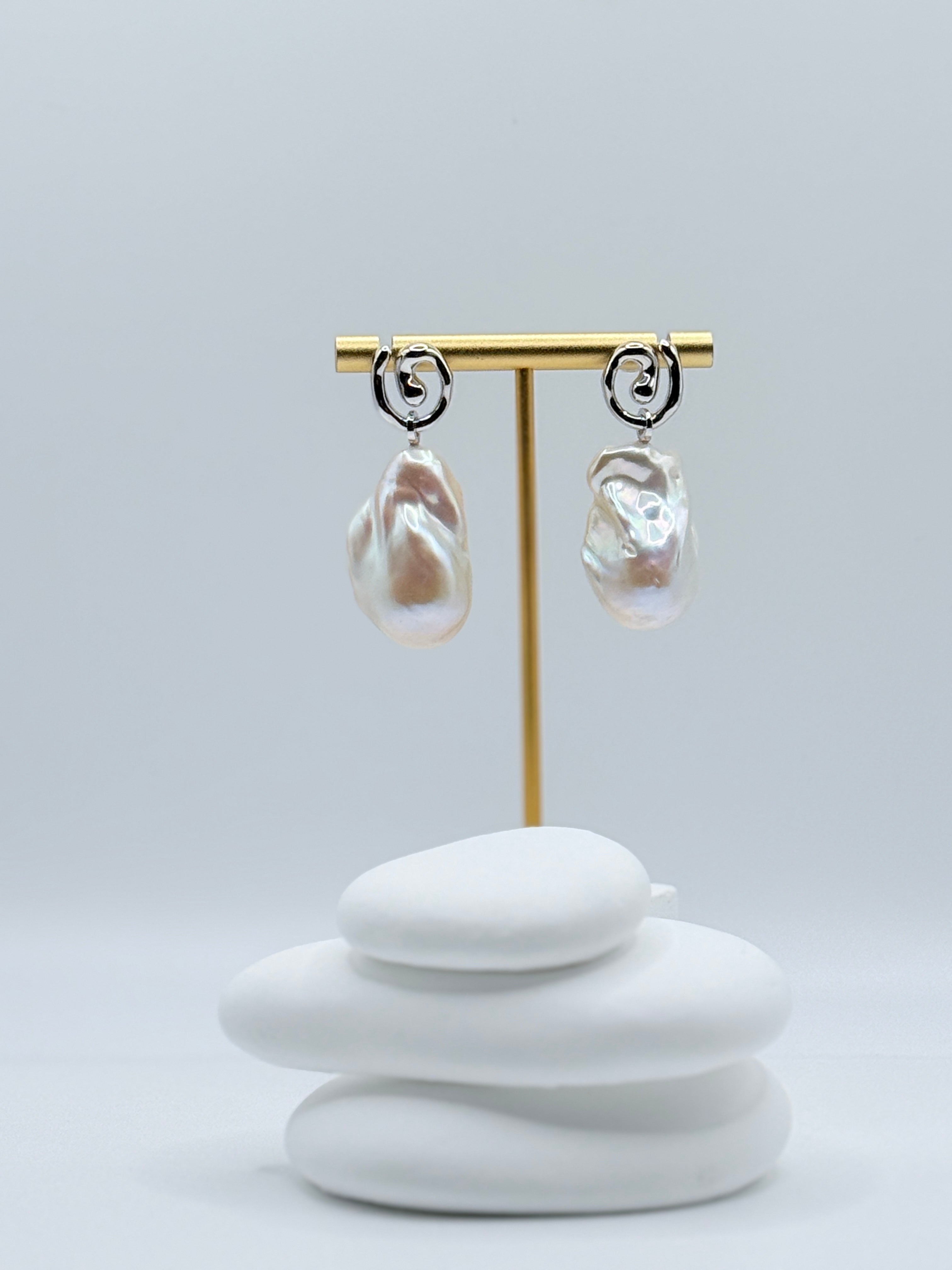 Sterling silver 2-way convertible dangle earrings with large baroque freshwater pearls and elegant curved elements displayed on gold earring stand
