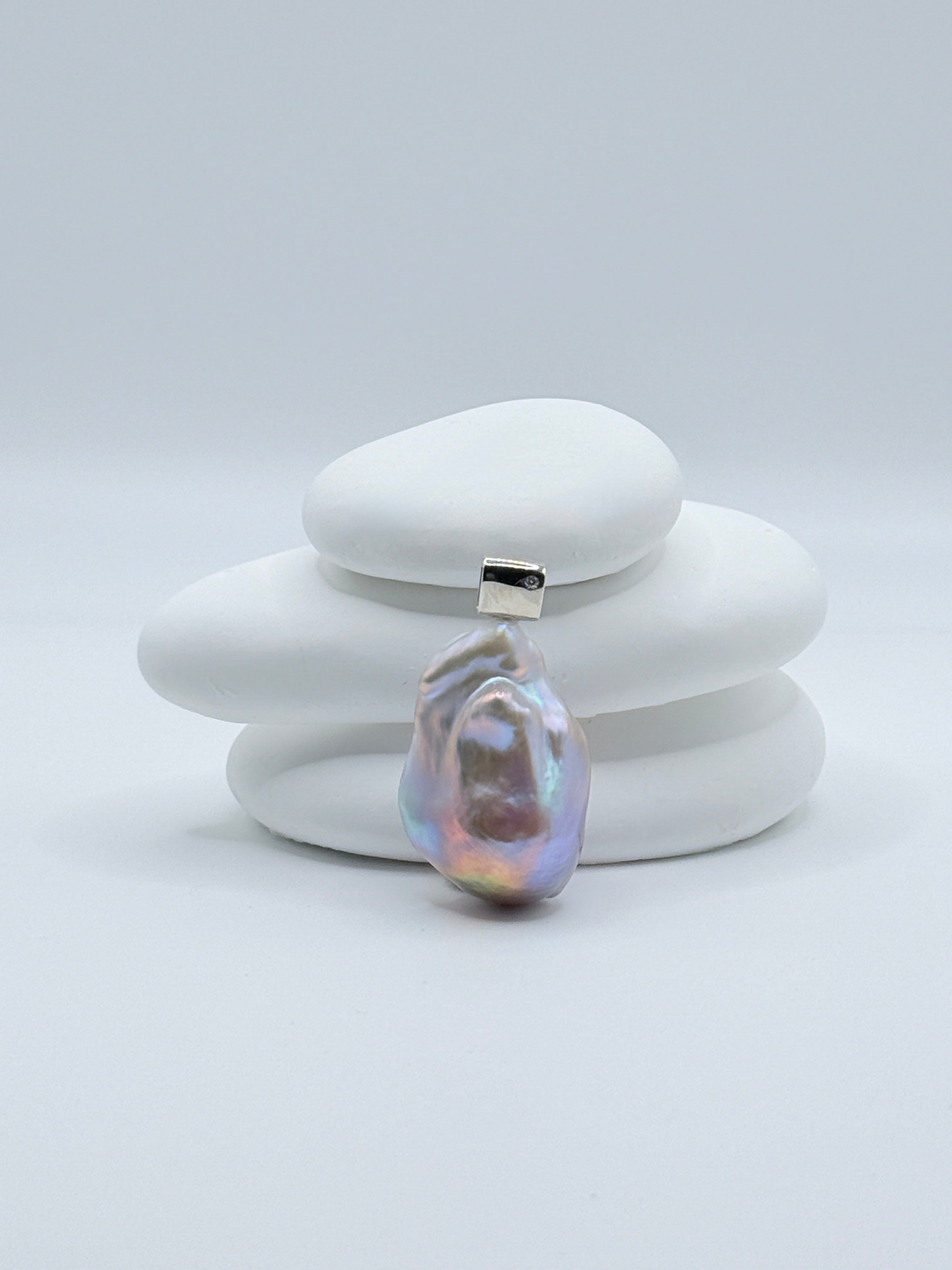 Large baroque freshwater pearl pendant with blue-purple rainbow iridescence and sterling silver CZ bail displayed on stacked white stones
