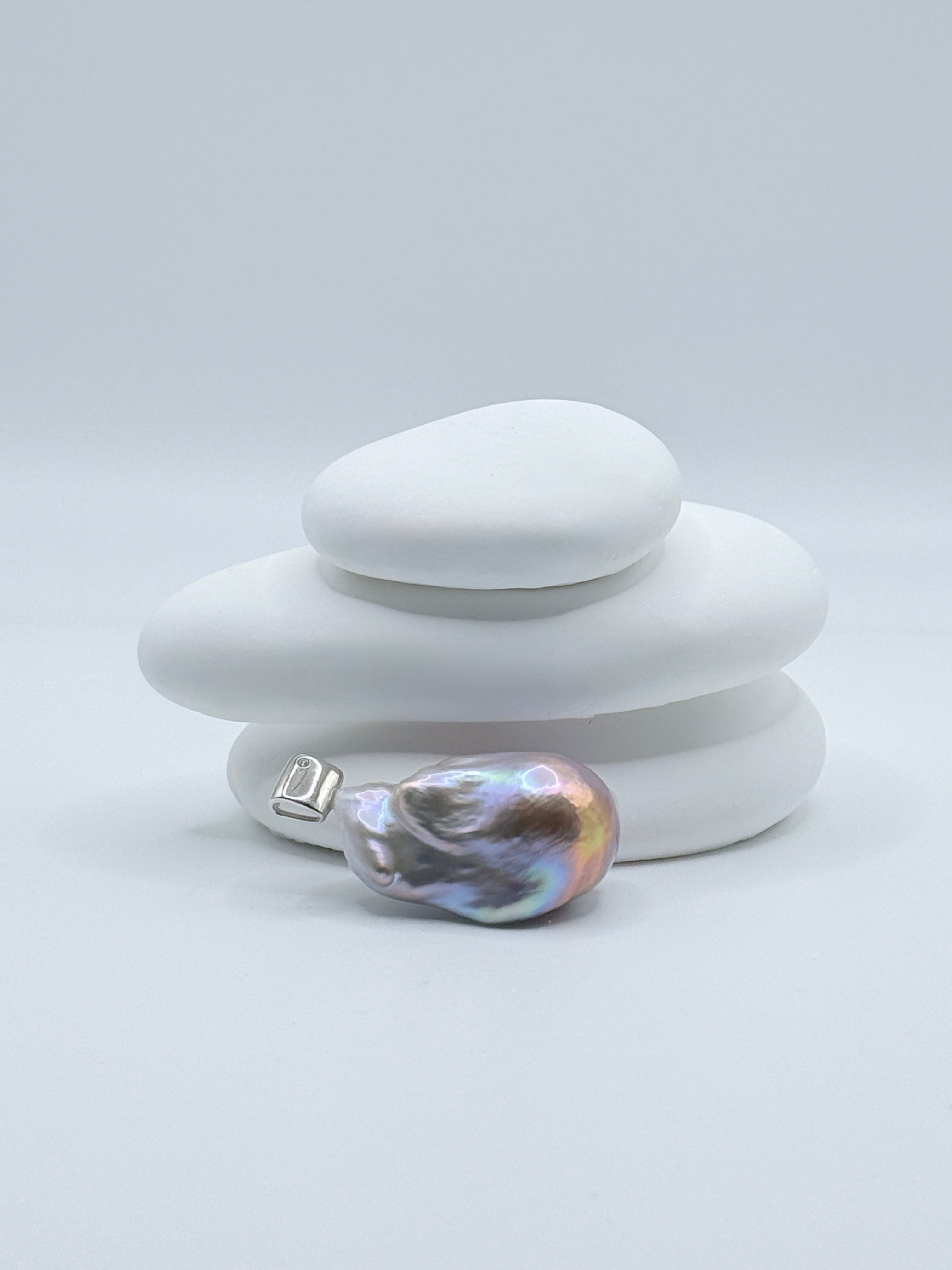 Sterling silver pendant with large baroque freshwater pearl showing blue-purple iridescence and CZ-set bail displayed on white stones
