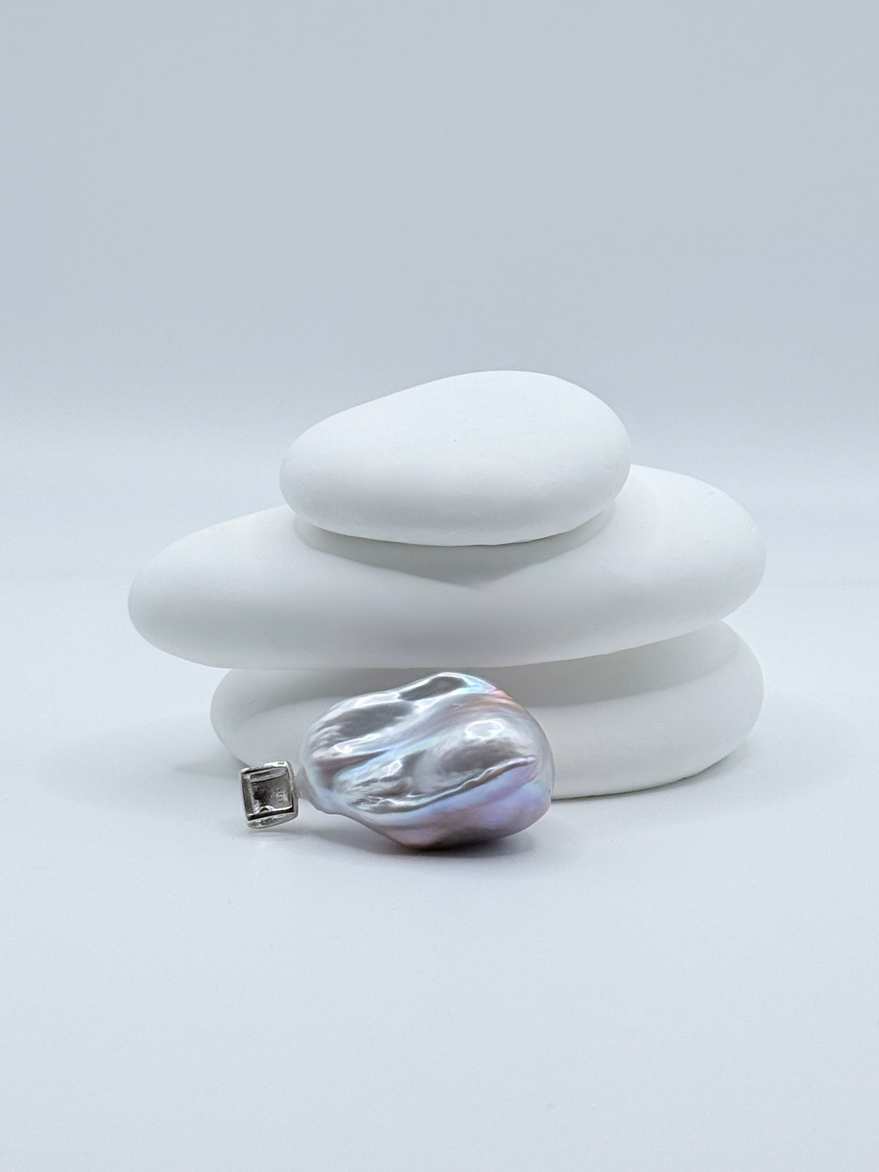 Close-up view of baroque freshwater pearl pendant with stunning iridescent colours and sterling silver bail with melee CZ on white stones