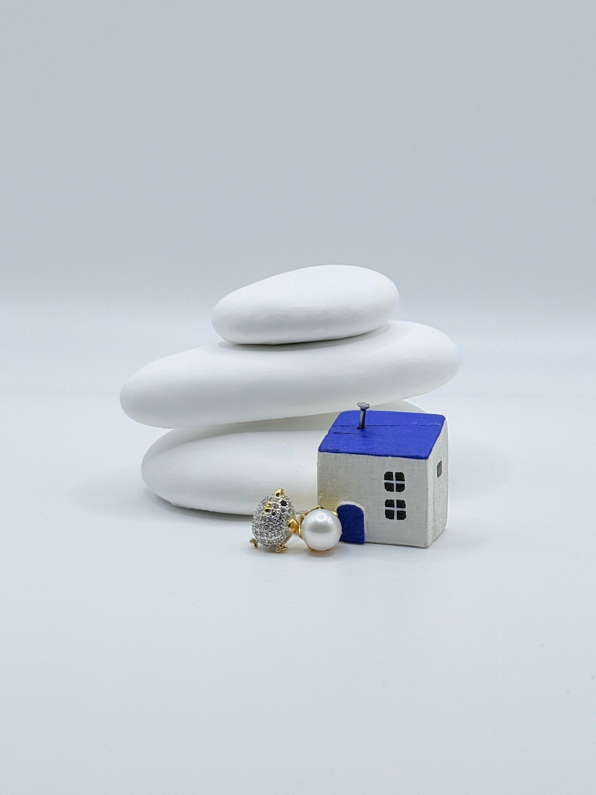 Gold plated sterling silver asymmetric ear studs with pavé CZ chick and white freshwater pearl egg displayed with decorative house on white stones