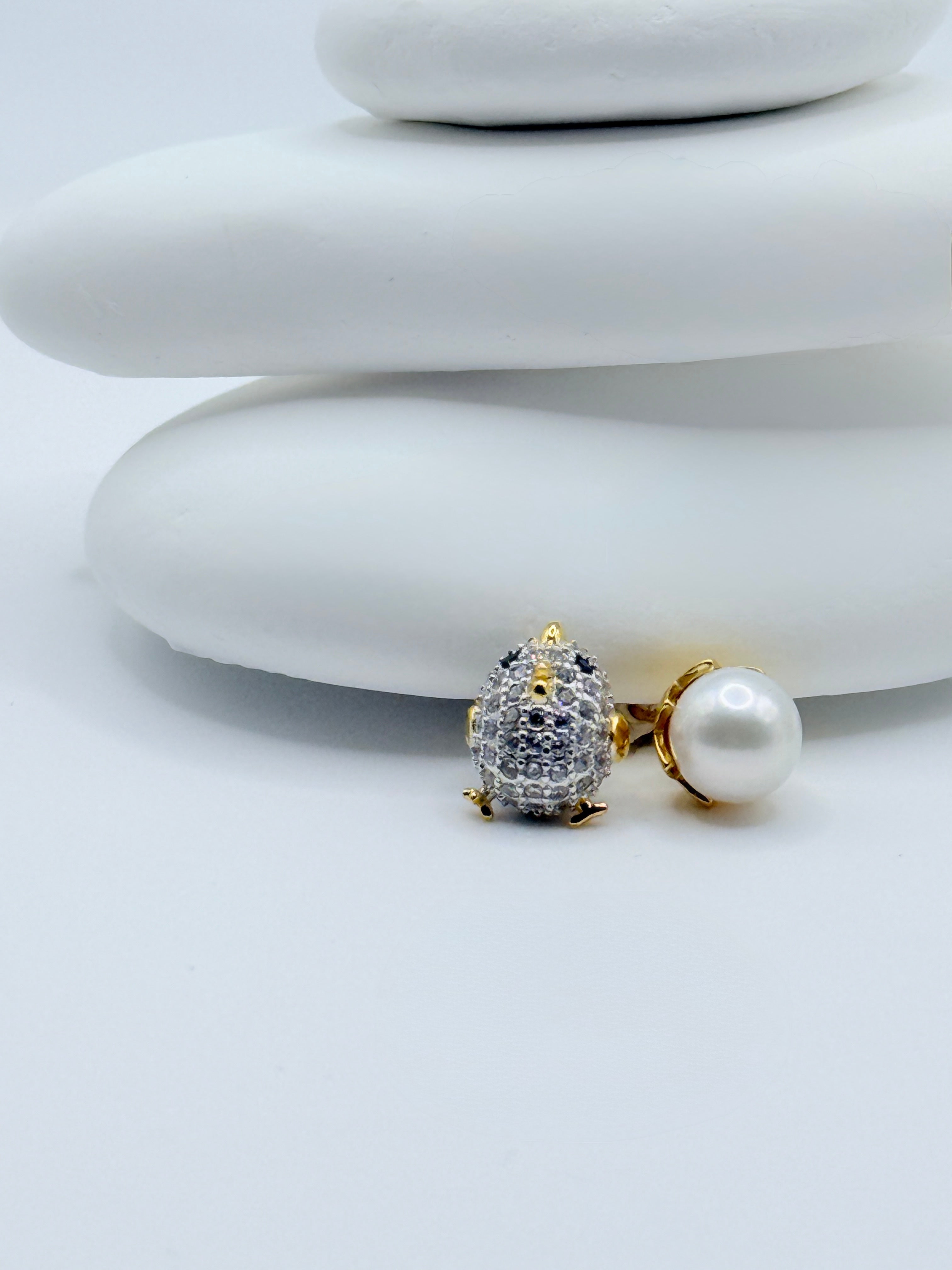 Close-up view of chick and egg ear studs showing pavé CZ details and white freshwater pearl on white stones with blue house decoration