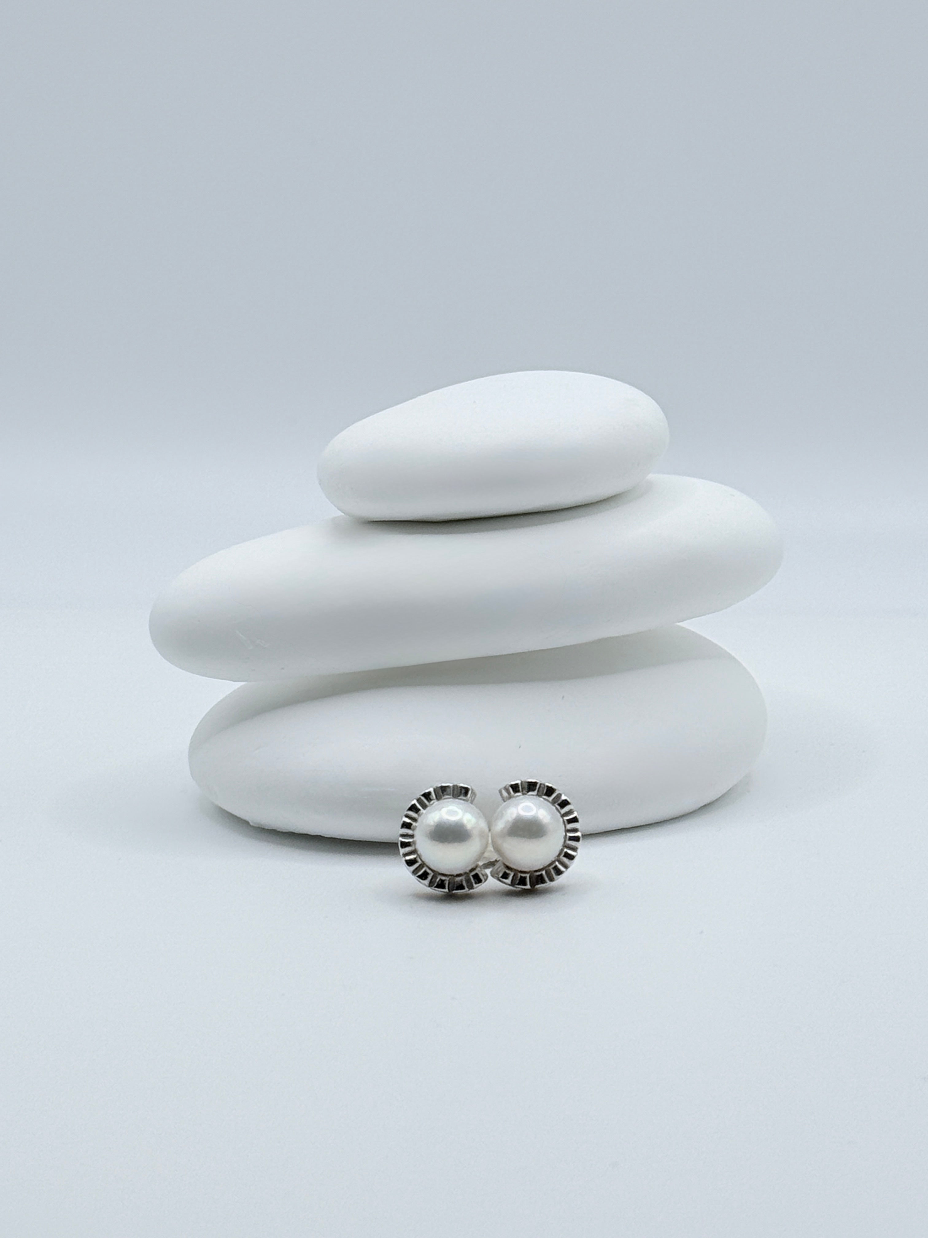 Sterling silver half halo ear studs with 8mm freshwater white round pearls displayed on white stone stack