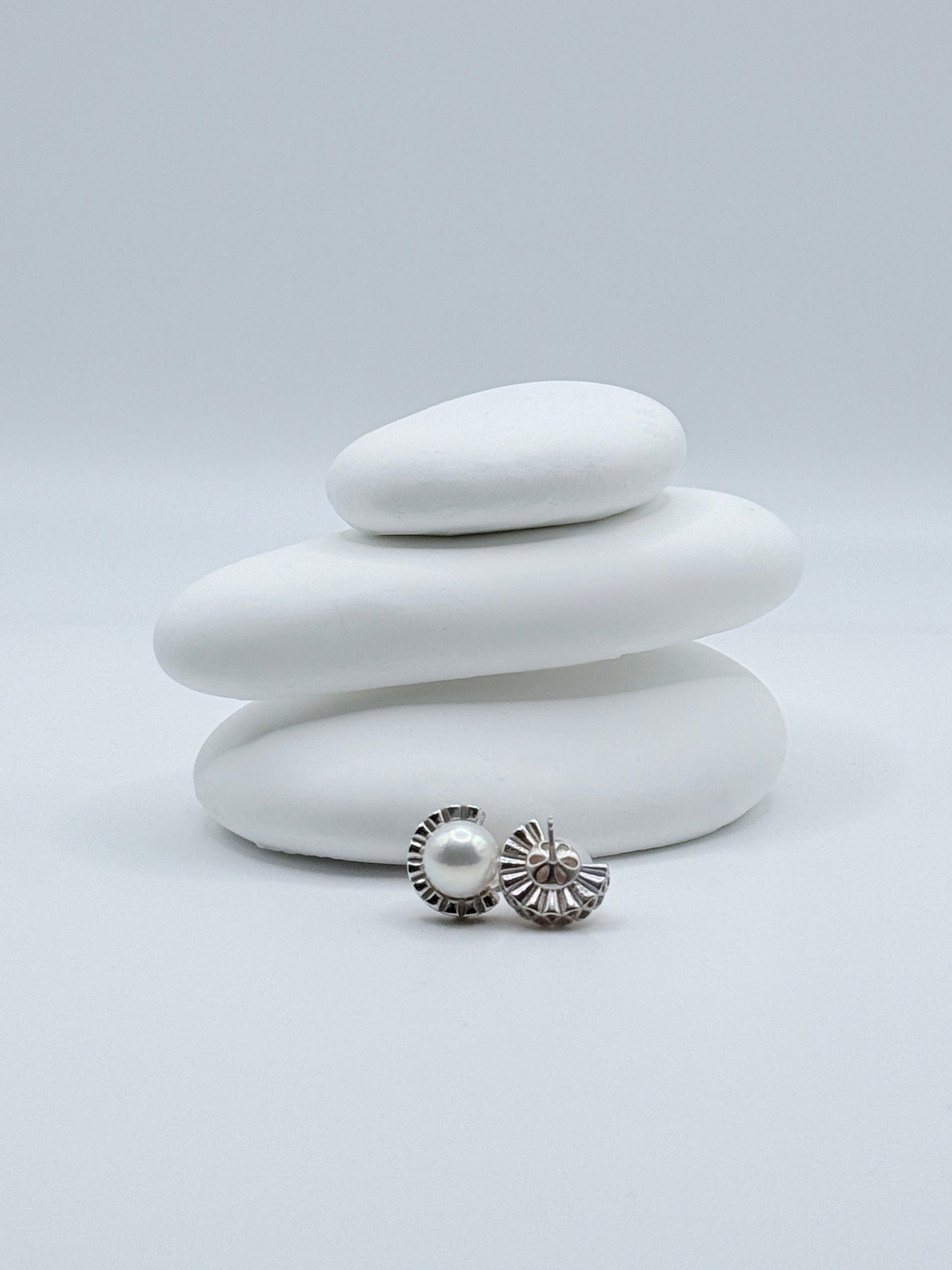 Close-up view of the back of sterling silver half halo ear studs showing architectural design with white freshwater round pearls on white stones