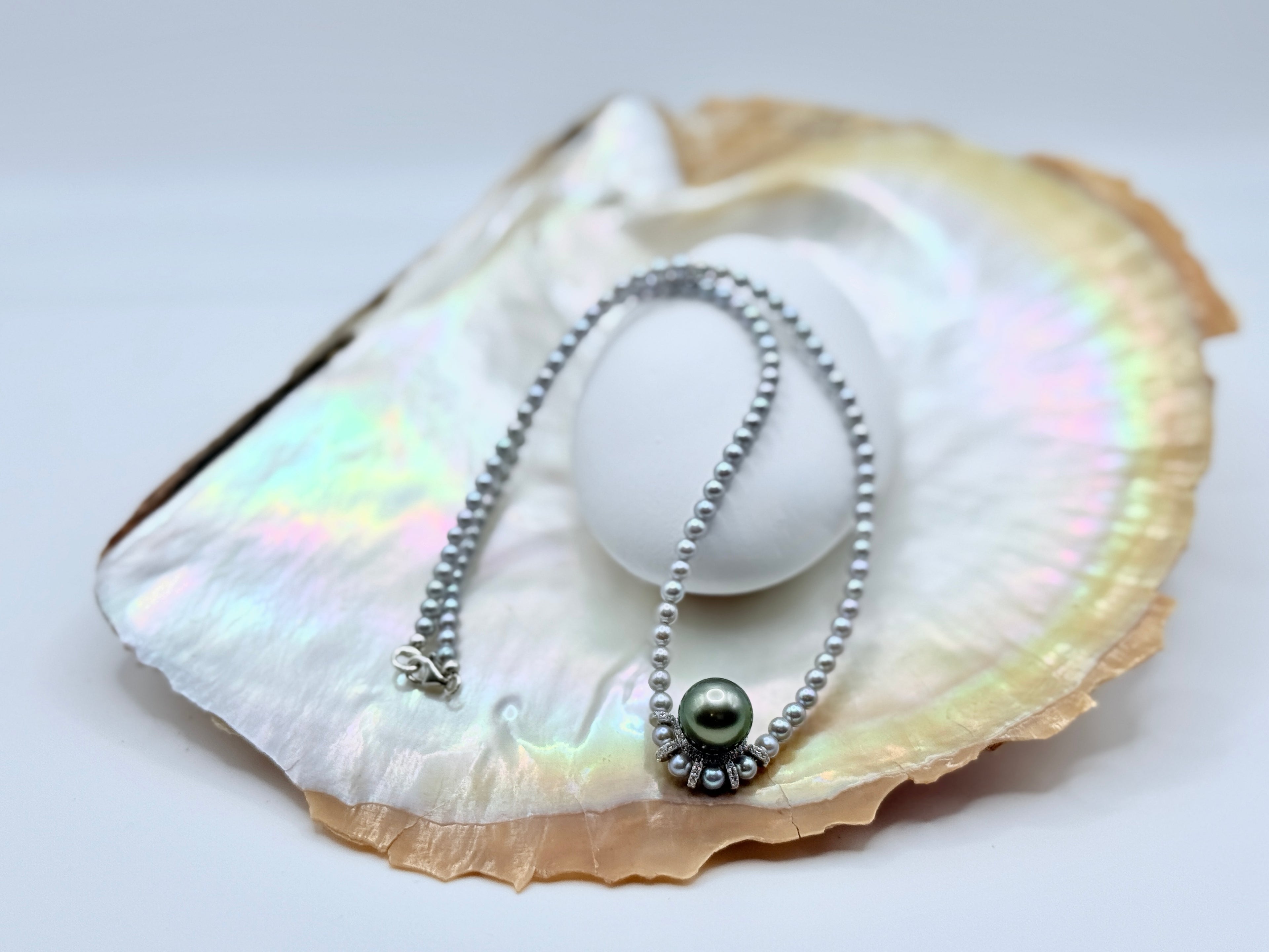 Grey freshwater seed pearl strand with green Tahitian pendant in decorative sterling silver setting on iridescent shell