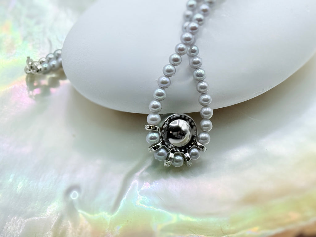 Green Tahitian pearl pendant detail showing decorative silver setting with grey freshwater seed pearl strand on iridescent shell