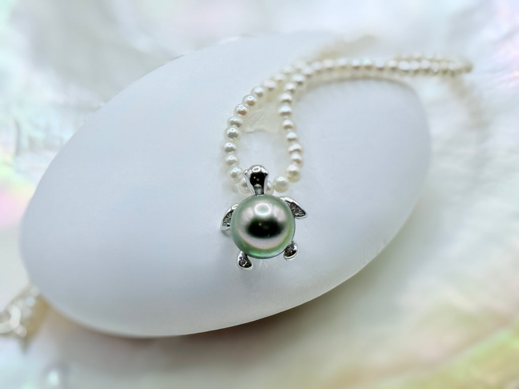 White freshwater seed pearl strand with green Tahitian sea turtle pendant in sterling silver on white shell and iridescent background