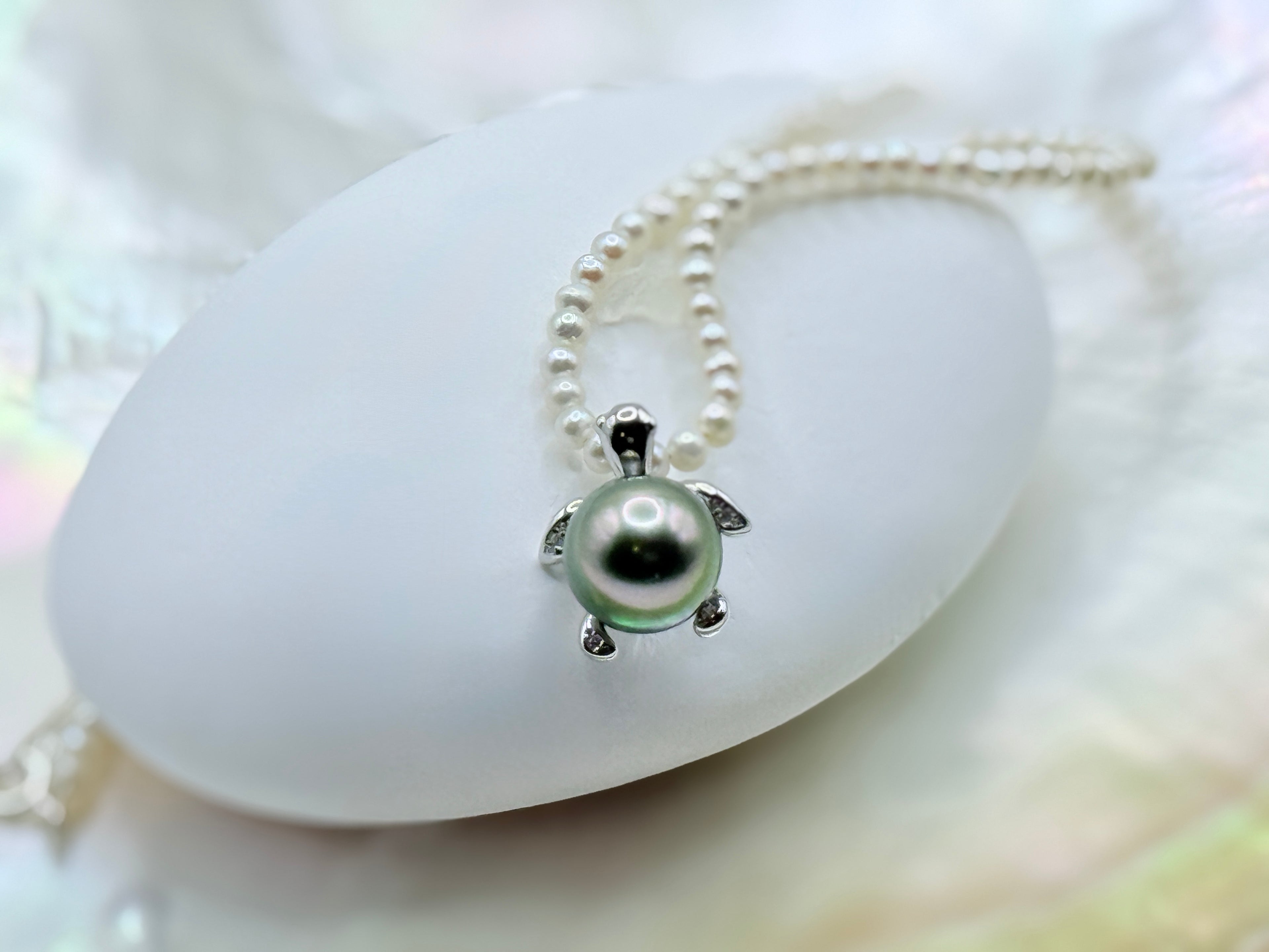 White freshwater seed pearl strand with green Tahitian sea turtle pendant in sterling silver on white shell and iridescent background