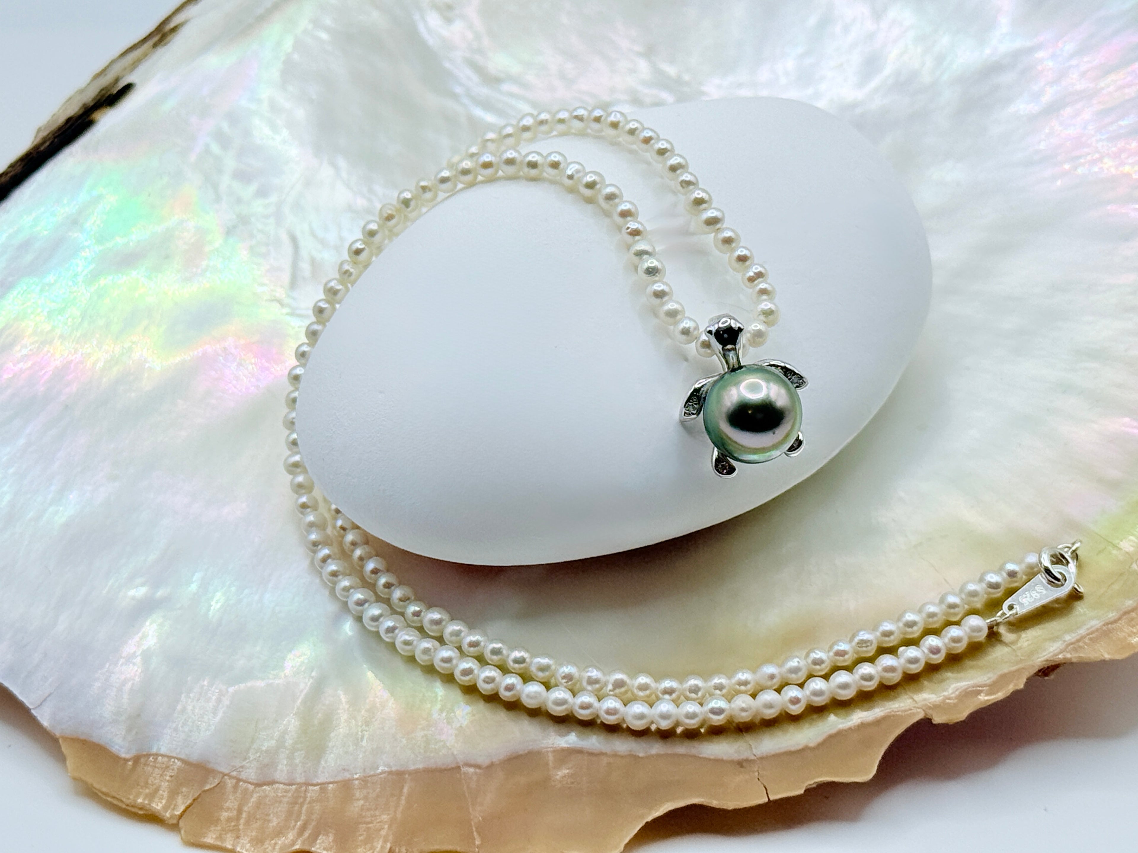 Detachable sea turtle pendant with green Tahitian pearl and white seed pearl strand showing hinged bail on shell and iridescent background