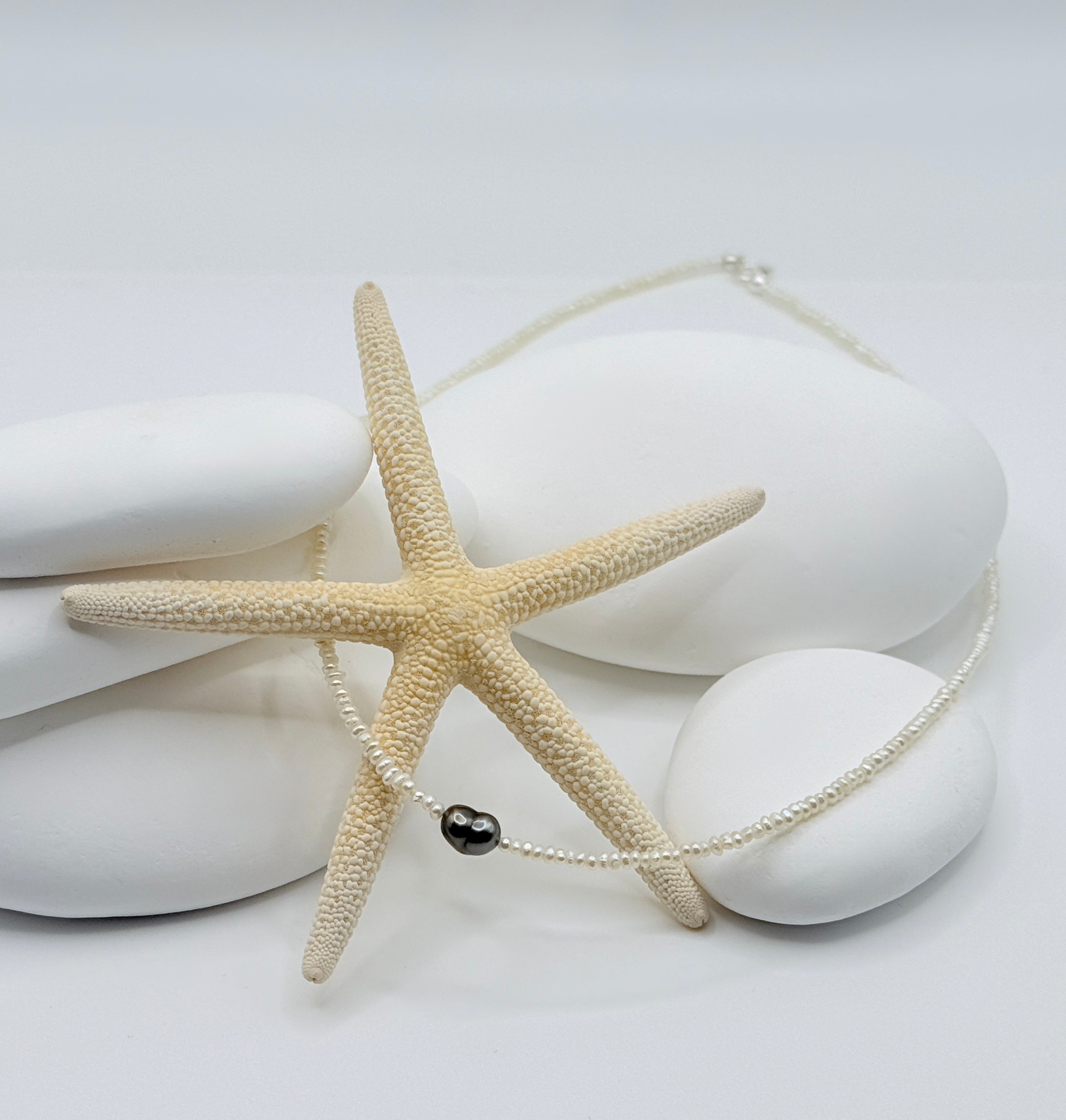 White freshwater seed pearl strand with heart-shaped Tahitian keshi pendant and sterling silver clasp on white shells and starfish