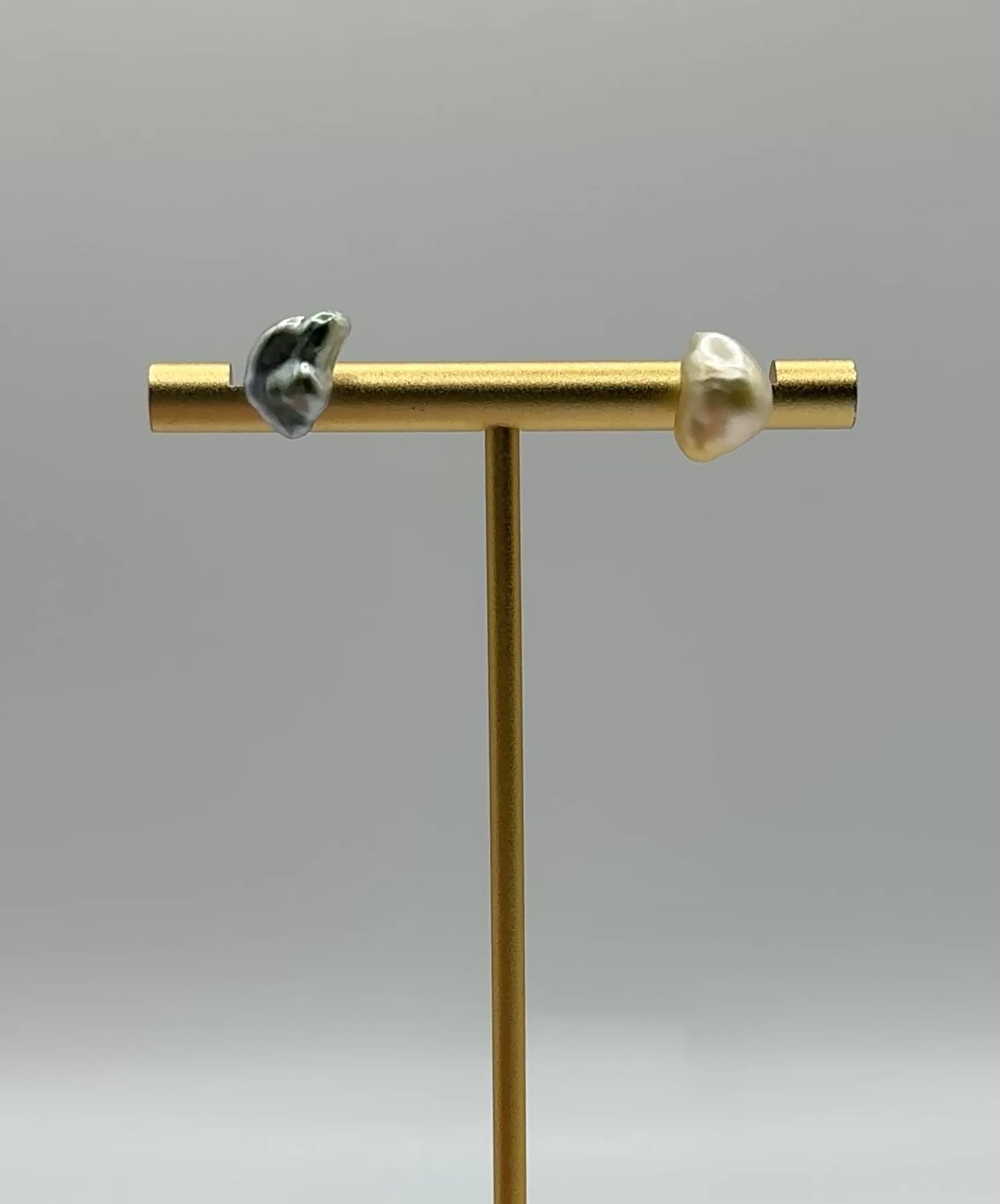 Half-moon Tahitian gold South Sea pearl stud earrings on stand rotating showing asymmetrical baroque crescent moon pearls golden and silvery-green tones