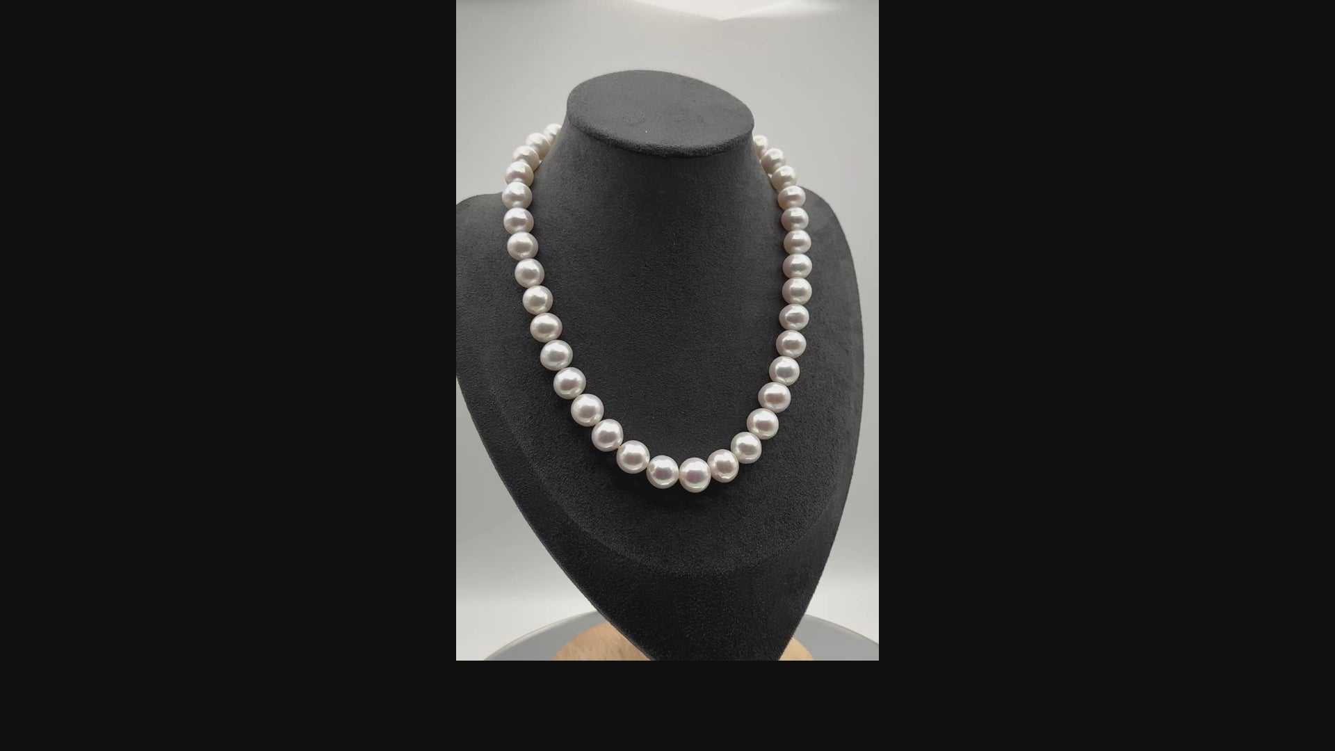 White freshwater pearl necklace with ornate infinity clasp rotating on display bust, showcasing the lustrous round pearls and decorative purple gemstone clasp from all angles