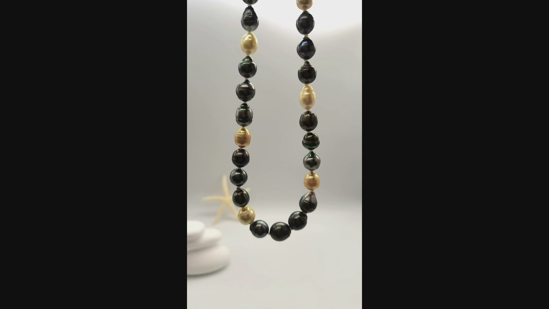 Video of multicoloured baroque pearl necklace suspended and gently moving in the air, displaying the beautiful variety of dark green, black, golden and white baroque pearls in fluid motion