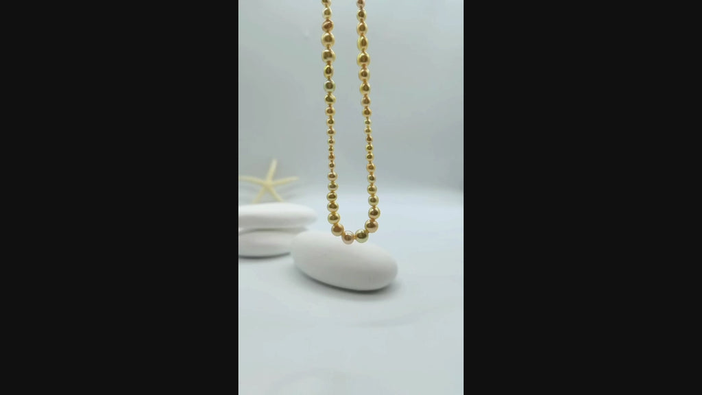 Video: Golden pearl strand necklace suspended and gently moving in the air, displaying the lustrous graduated pearls and fluid drape of the complete necklace design