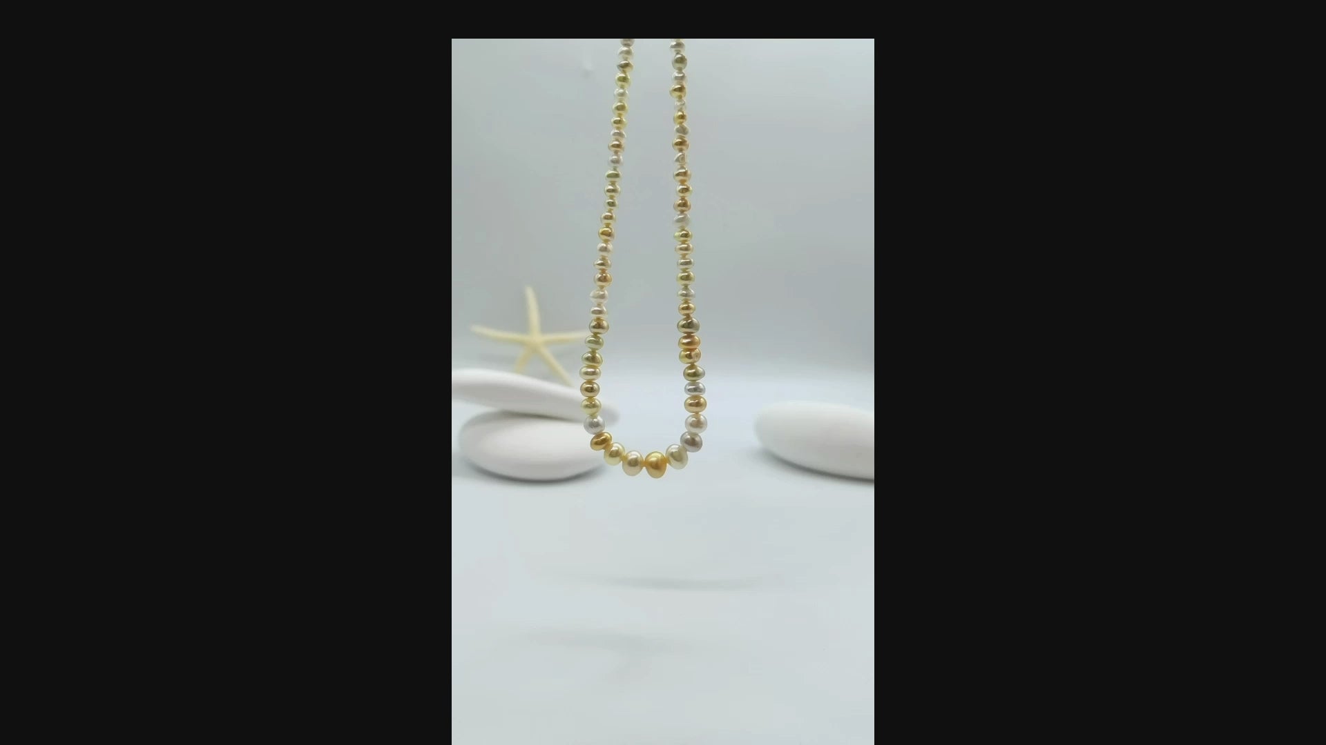 White and cream pearl strand necklace suspended and gently moving in the air, displaying the lustrous graduated pearls and graceful movement of the complete necklace design