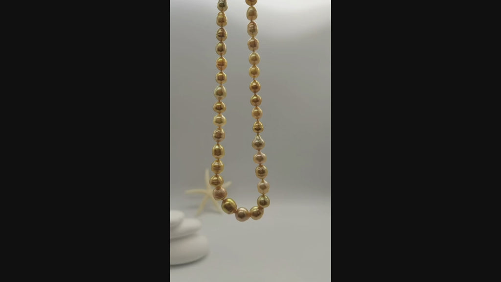 Golden baroque pearl necklace suspended and gently moving in the air, displaying the lustrous graduated pearls and natural baroque shapes in fluid motion