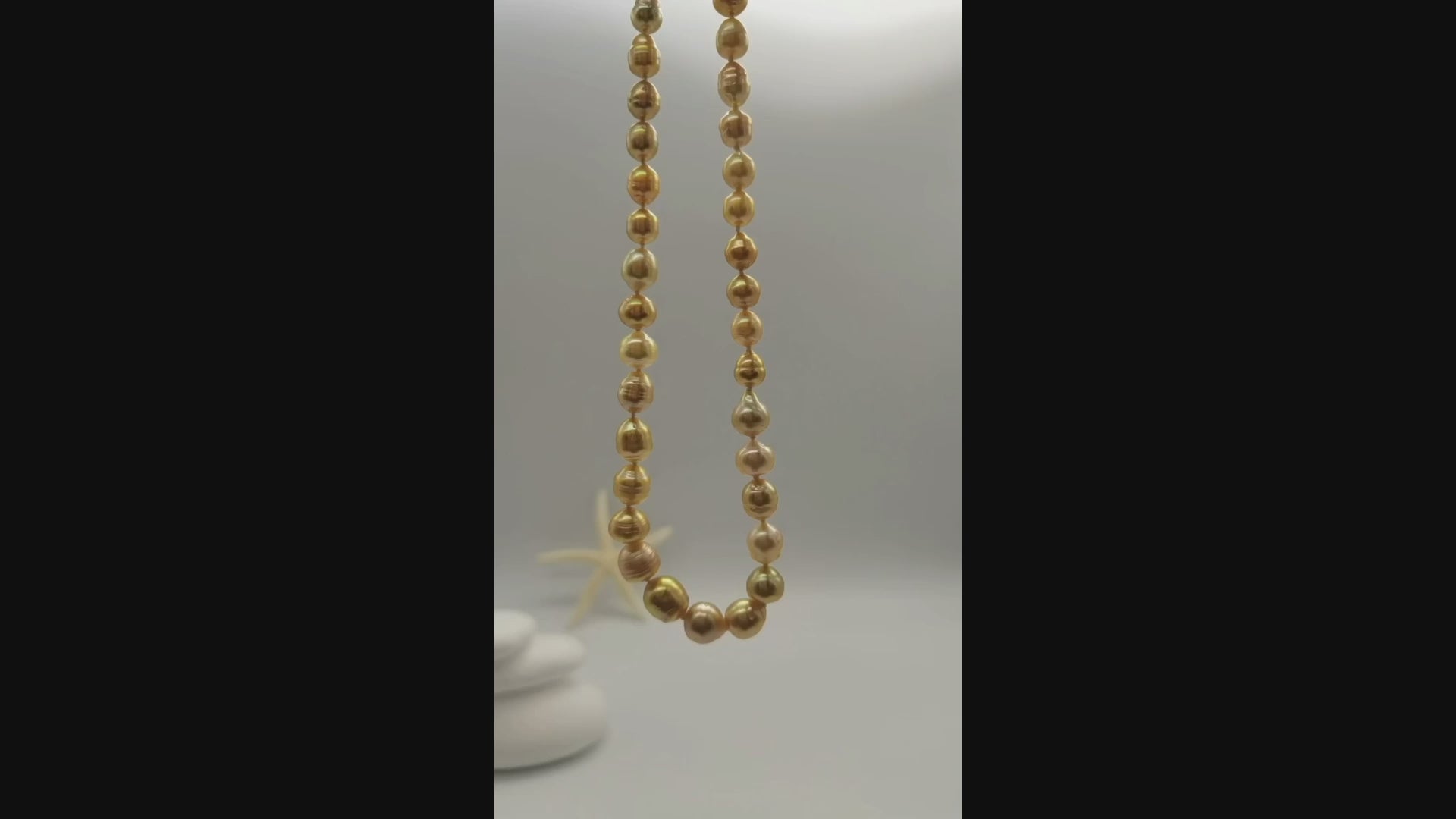 Golden baroque pearl necklace suspended and gently moving in the air, displaying the lustrous graduated pearls and natural baroque shapes in fluid motion